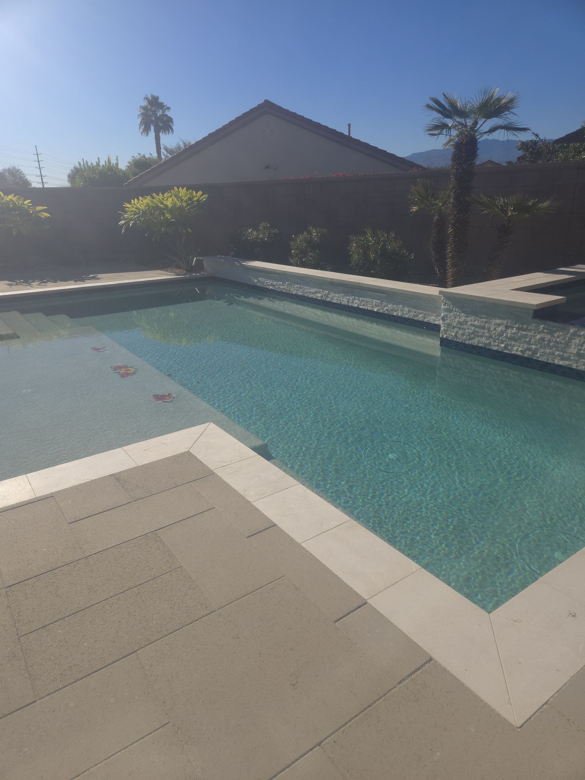 Pool with light blue water and stone patio under a clear blue sky.