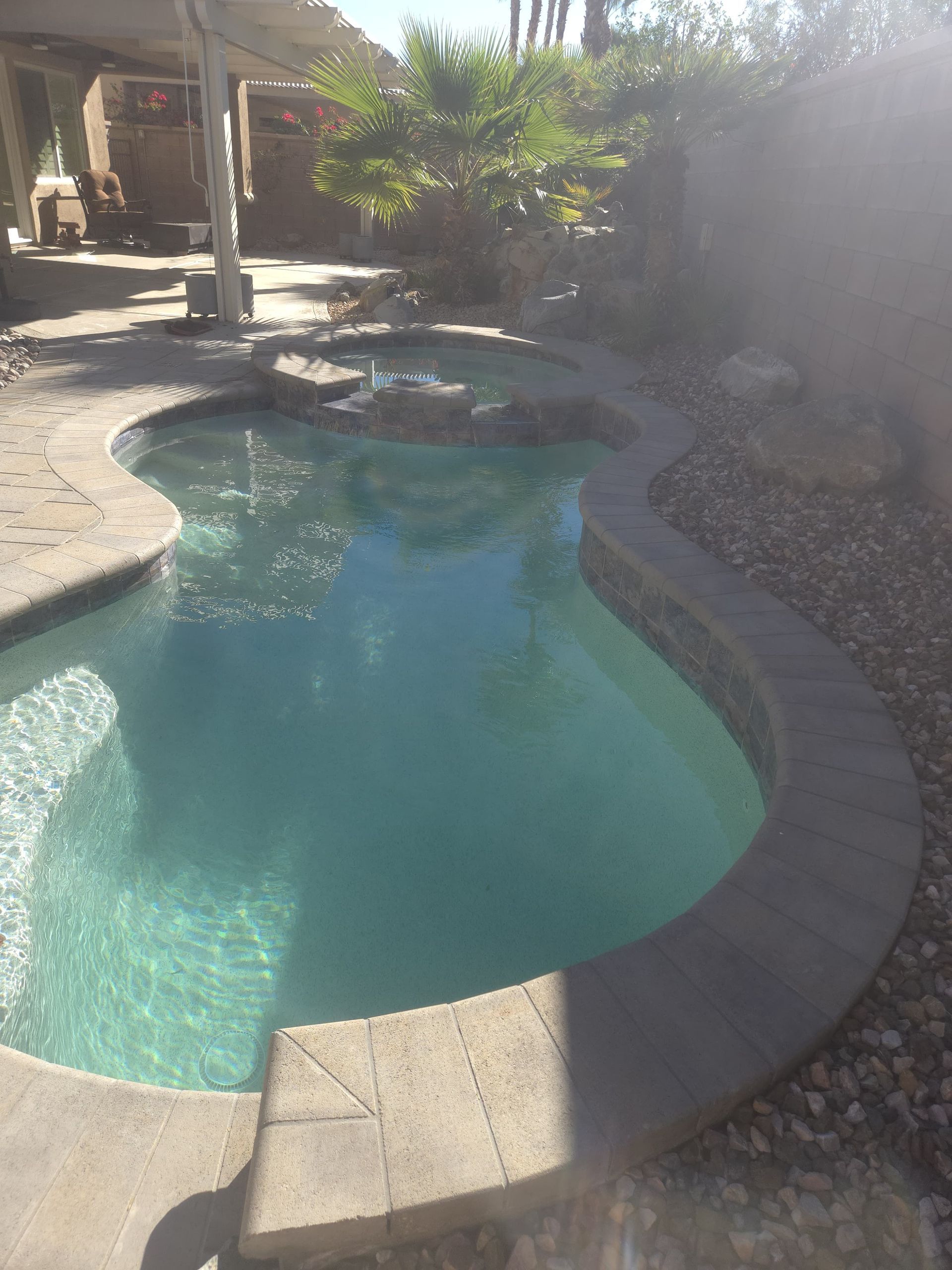 Pool with turquoise water, a curved edge, and small stones beside it, sunny outdoor setting.