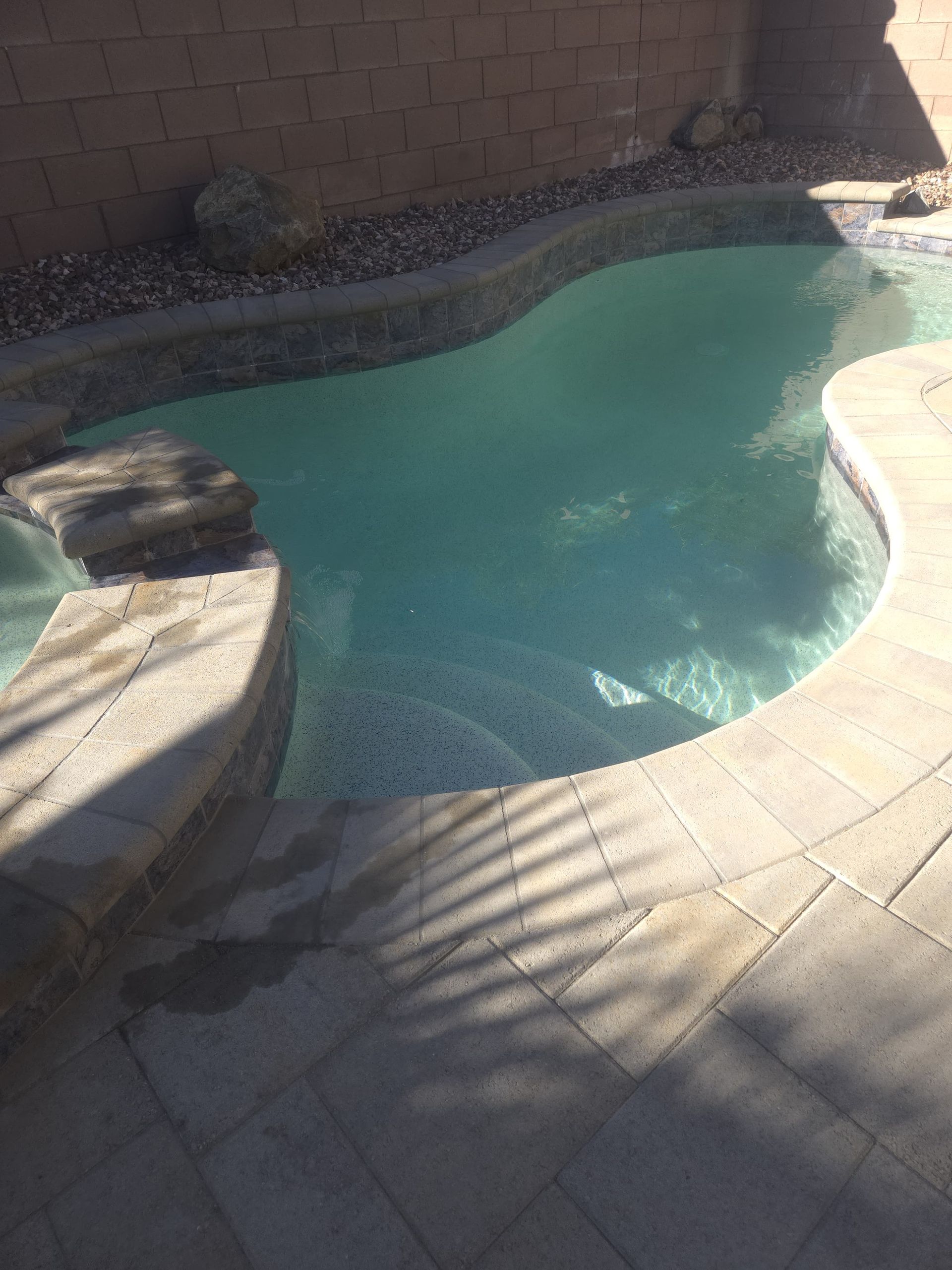 Pool with light blue water and stone steps and surrounding patio.
