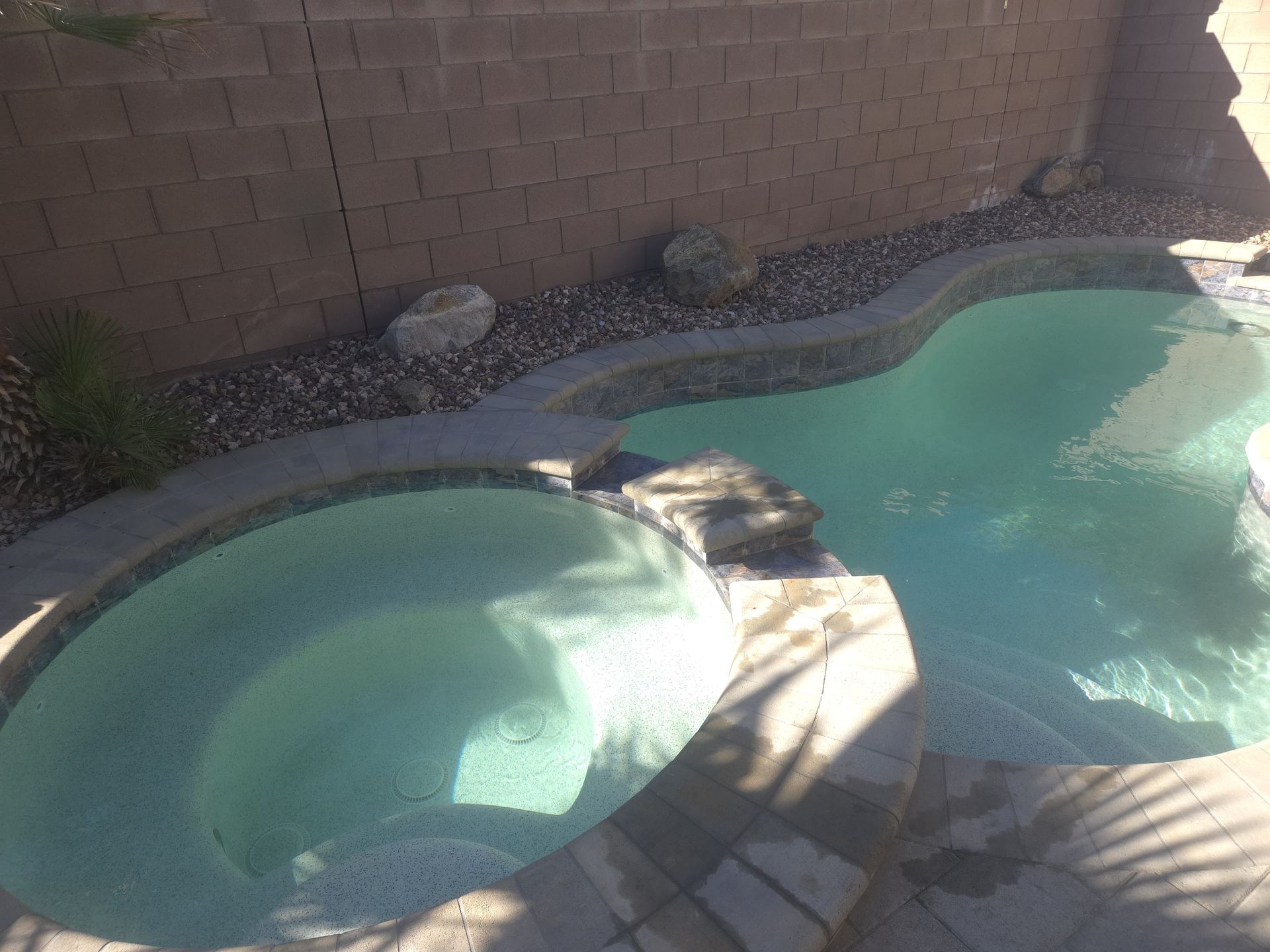 Swimming pool with attached spa and stone landscaping along a brick wall.