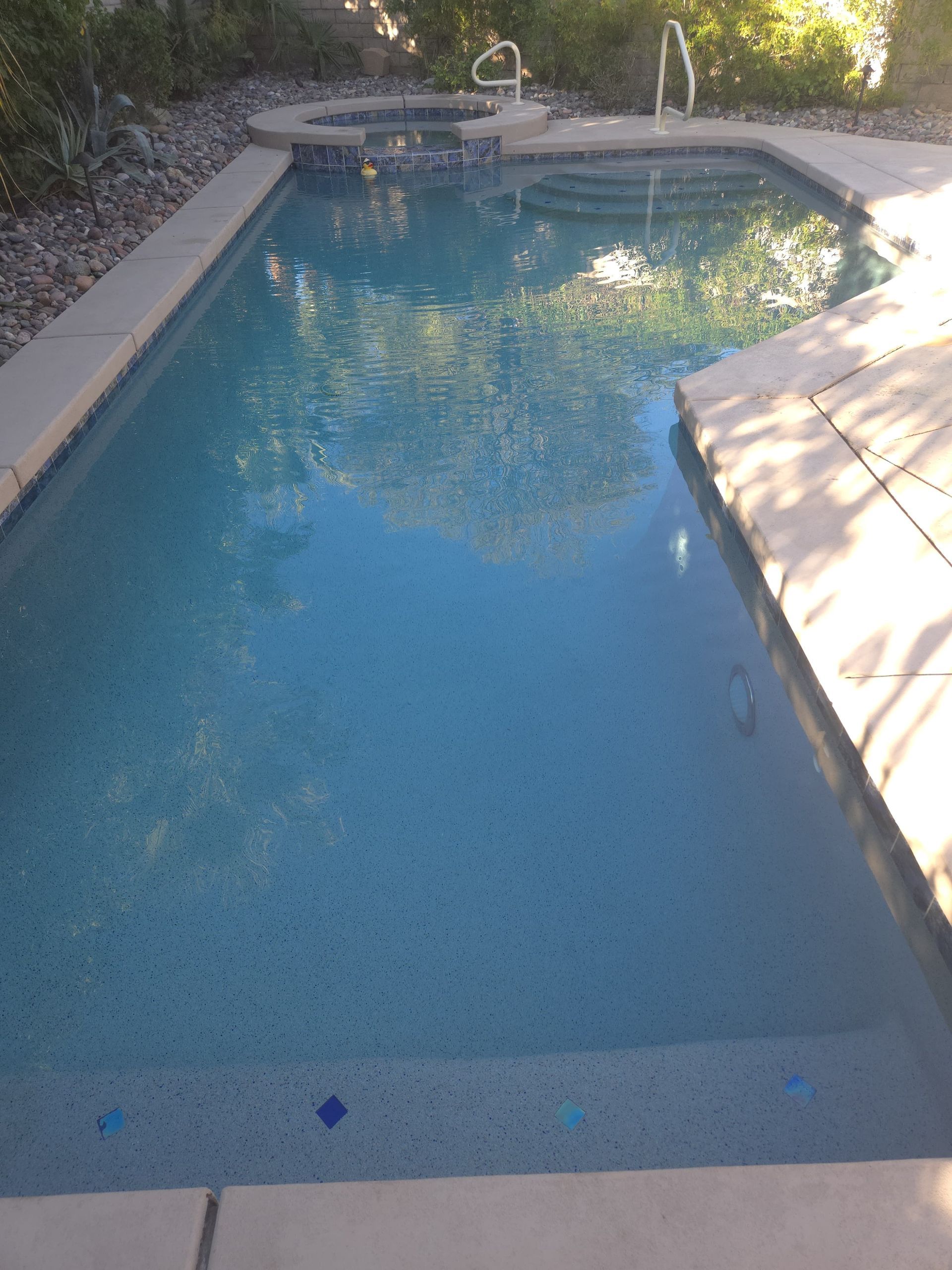 Pool with blue water and surrounding stone deck. Small hot tub to the side.