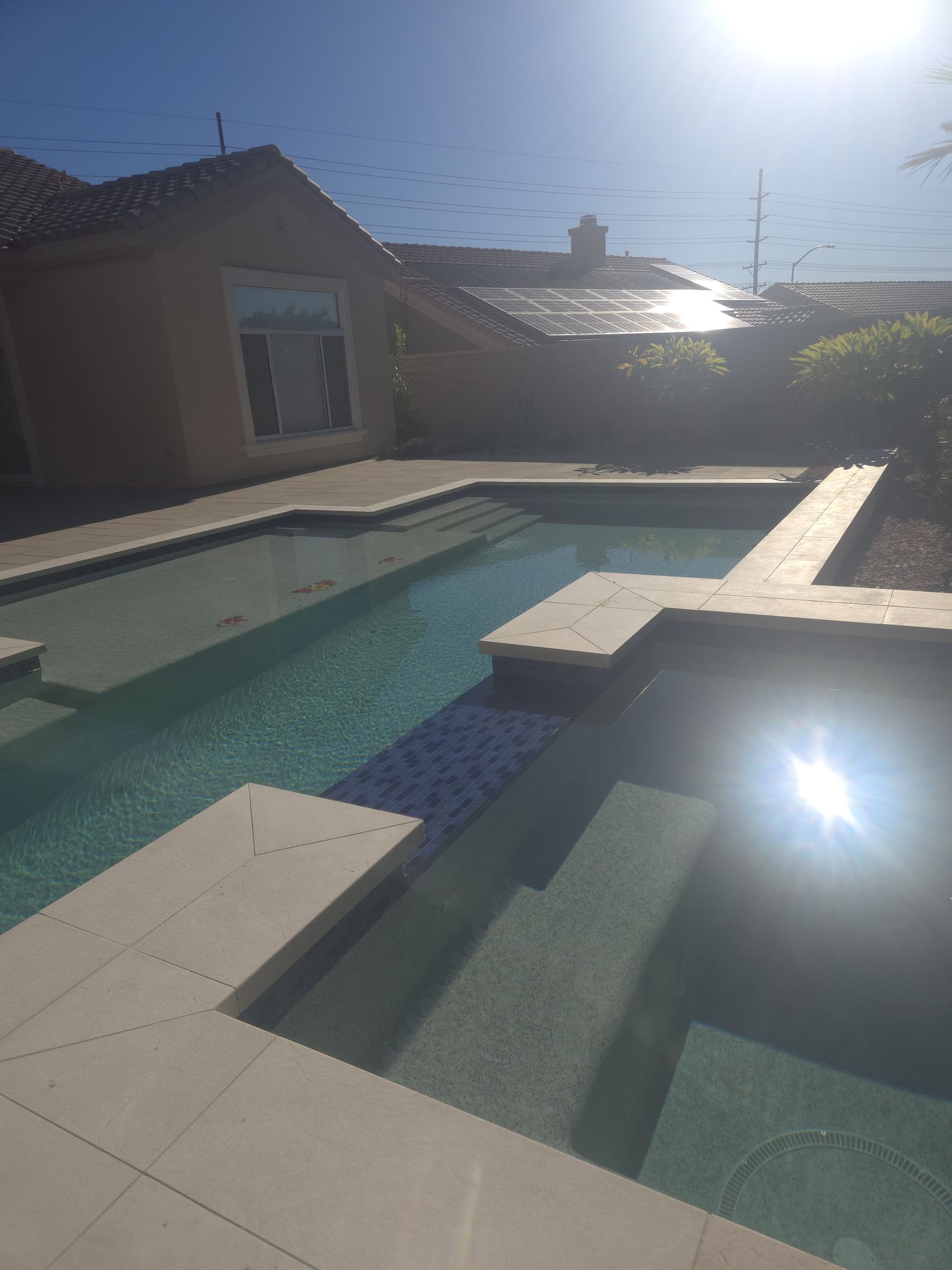 A multi-level swimming pool with a house in the background on a sunny day.