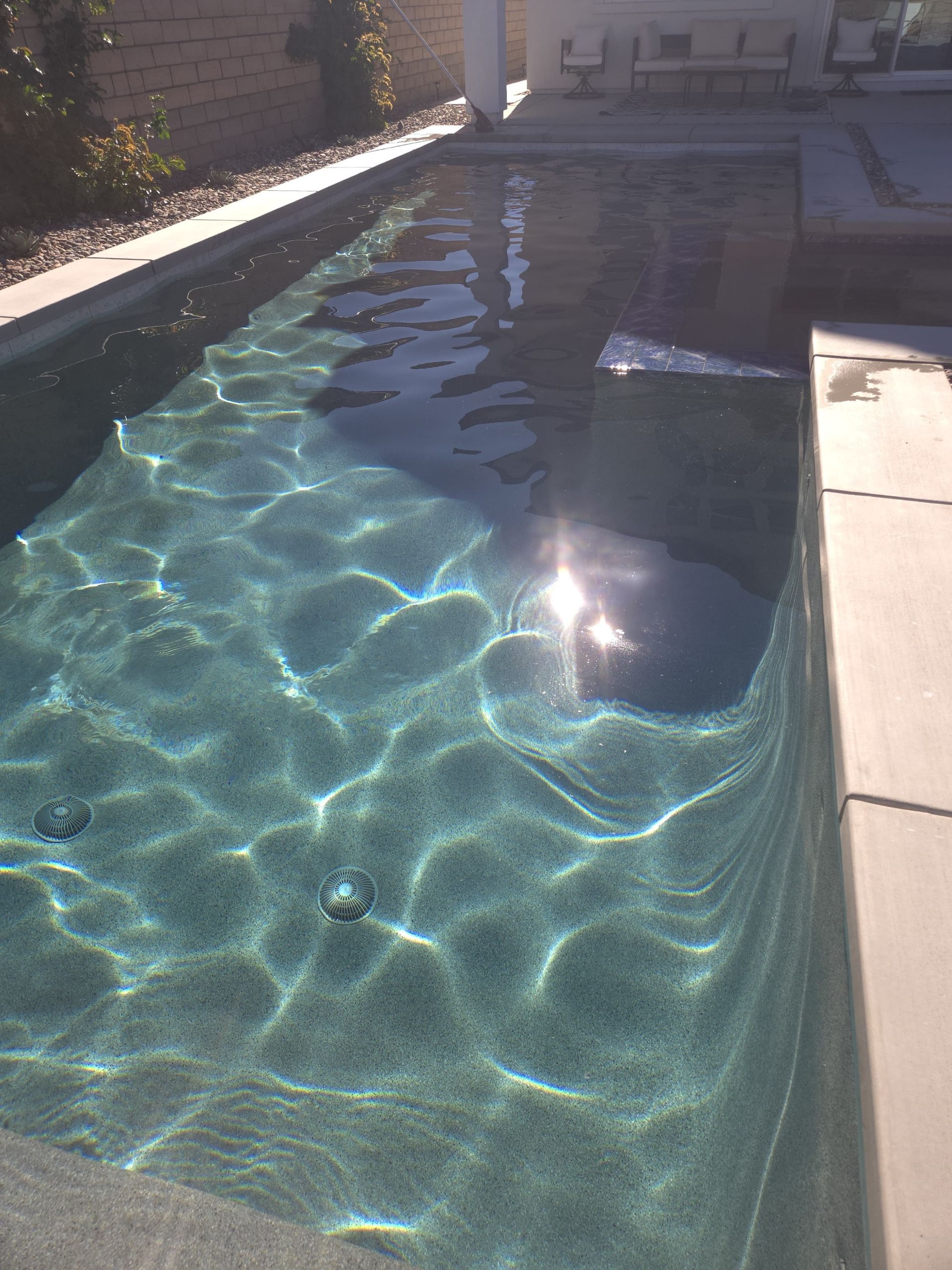 Rectangular swimming pool with shimmering turquoise water, bright sunlight reflection.