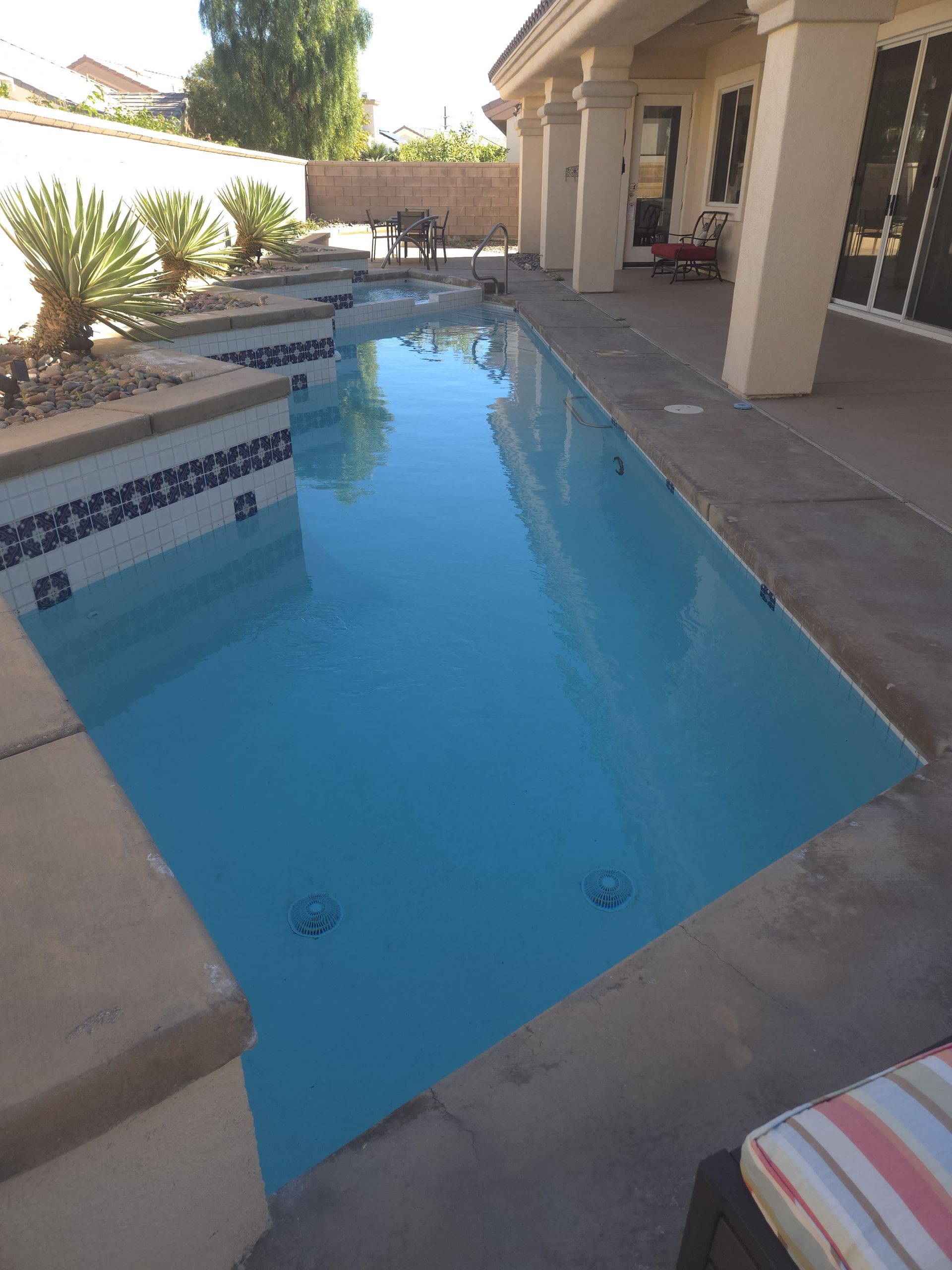 Long, rectangular swimming pool with blue water next to a covered patio.