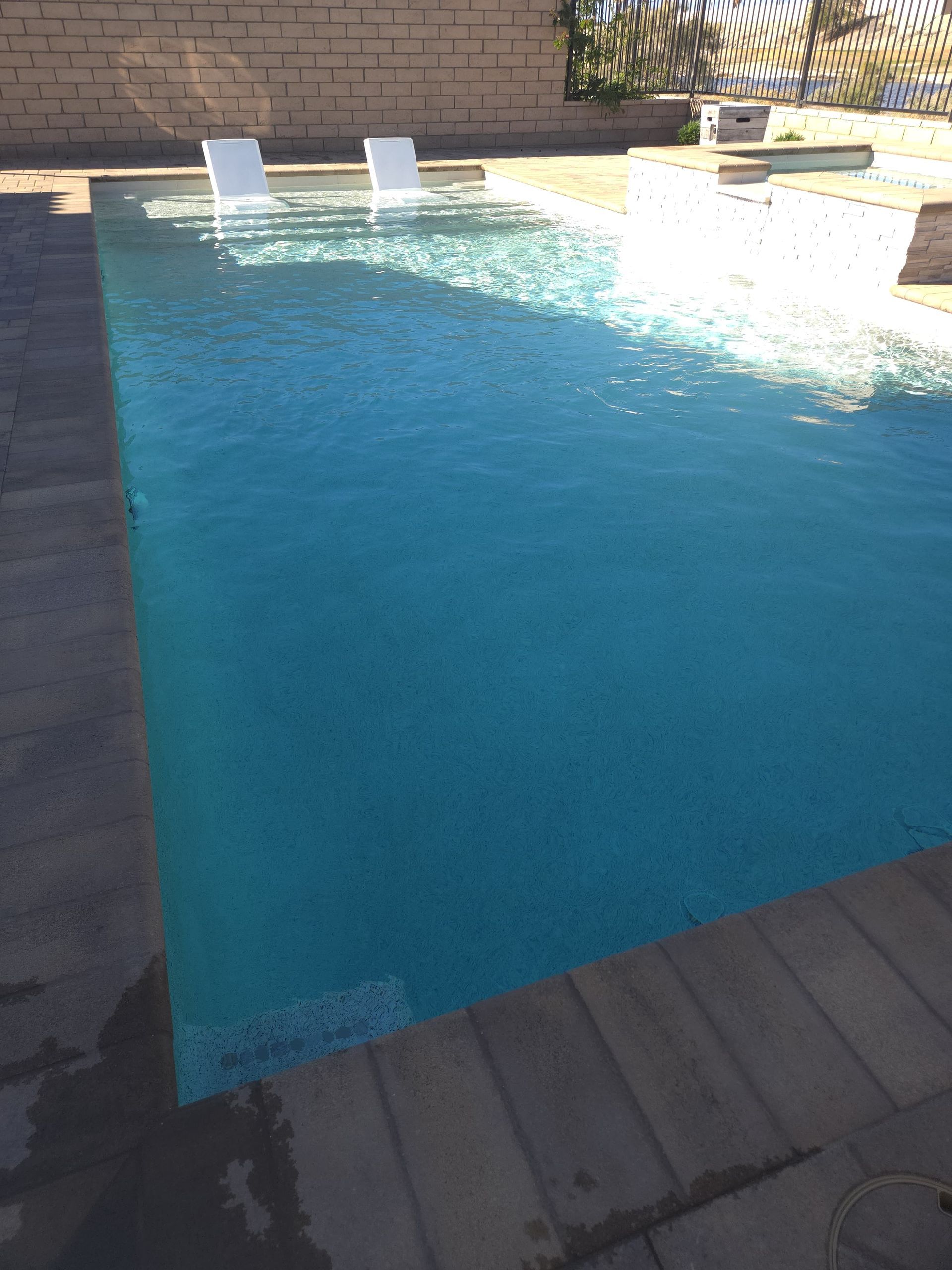 Rectangular pool with clear blue water and two white lounge chairs; outdoors.