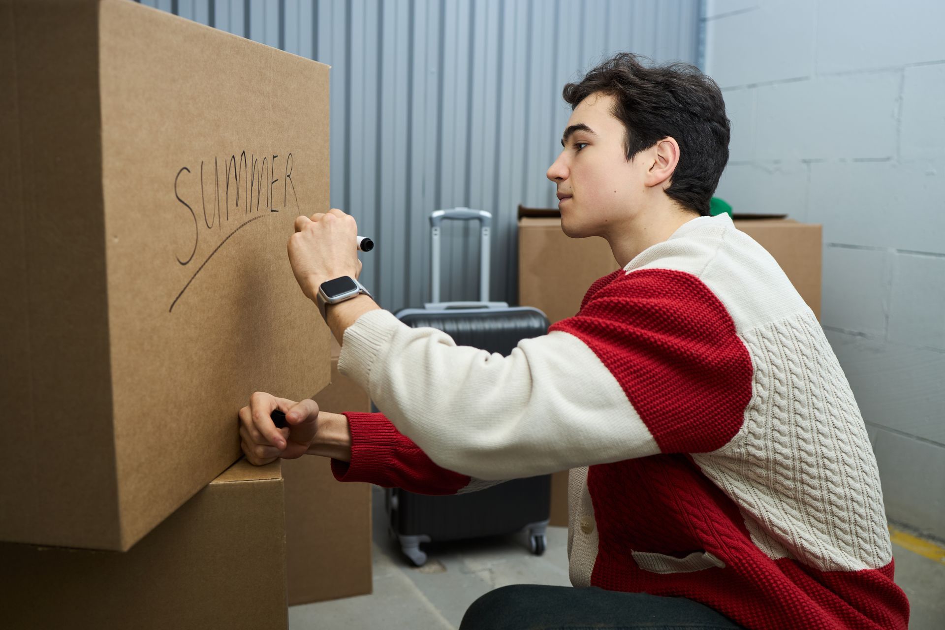 Man writing on a cardboard box labeled “SHIRTS” in a moving room