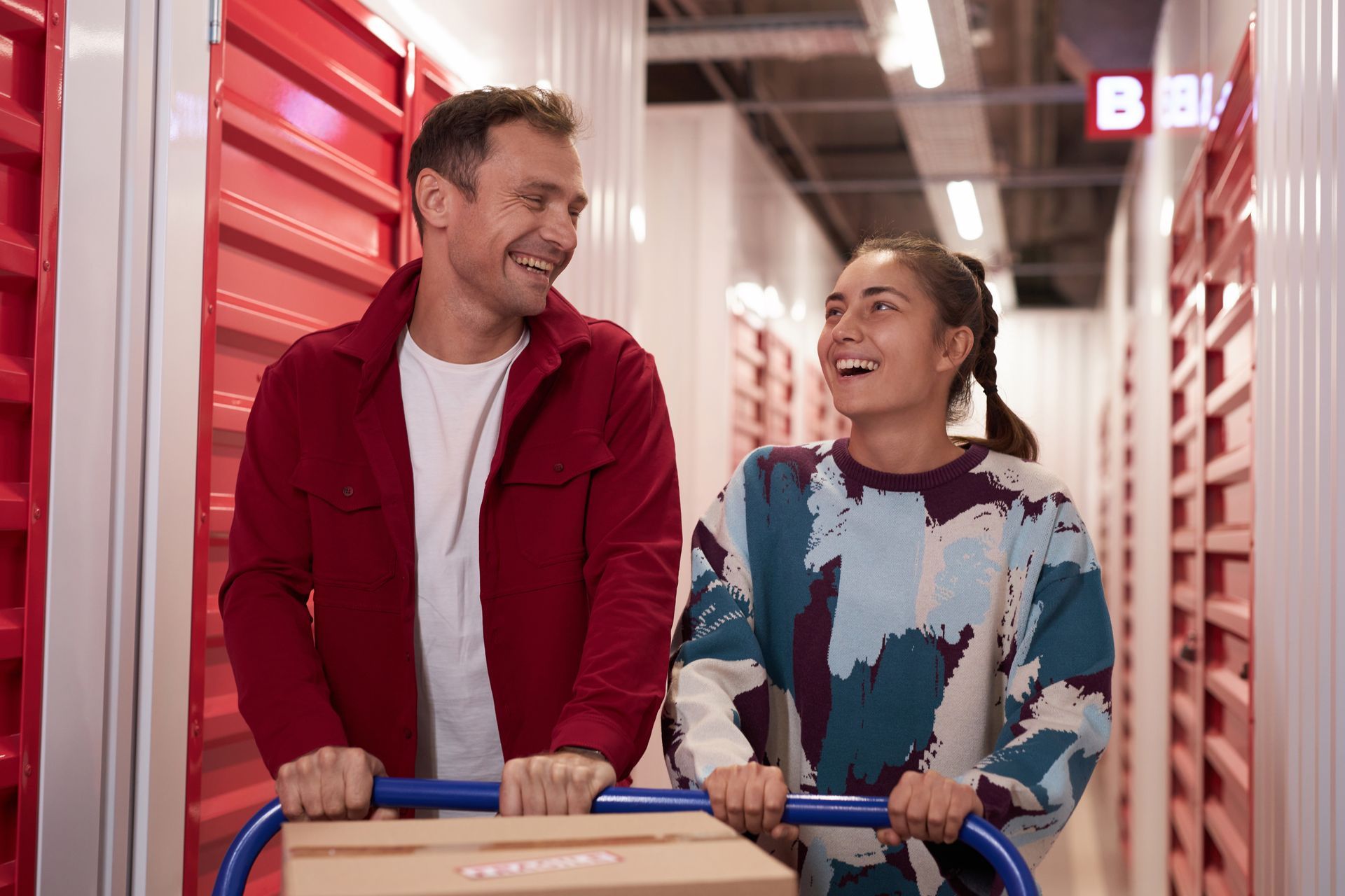 Two smiling shoppers pushing a cart down a store aisle lined with red lockers