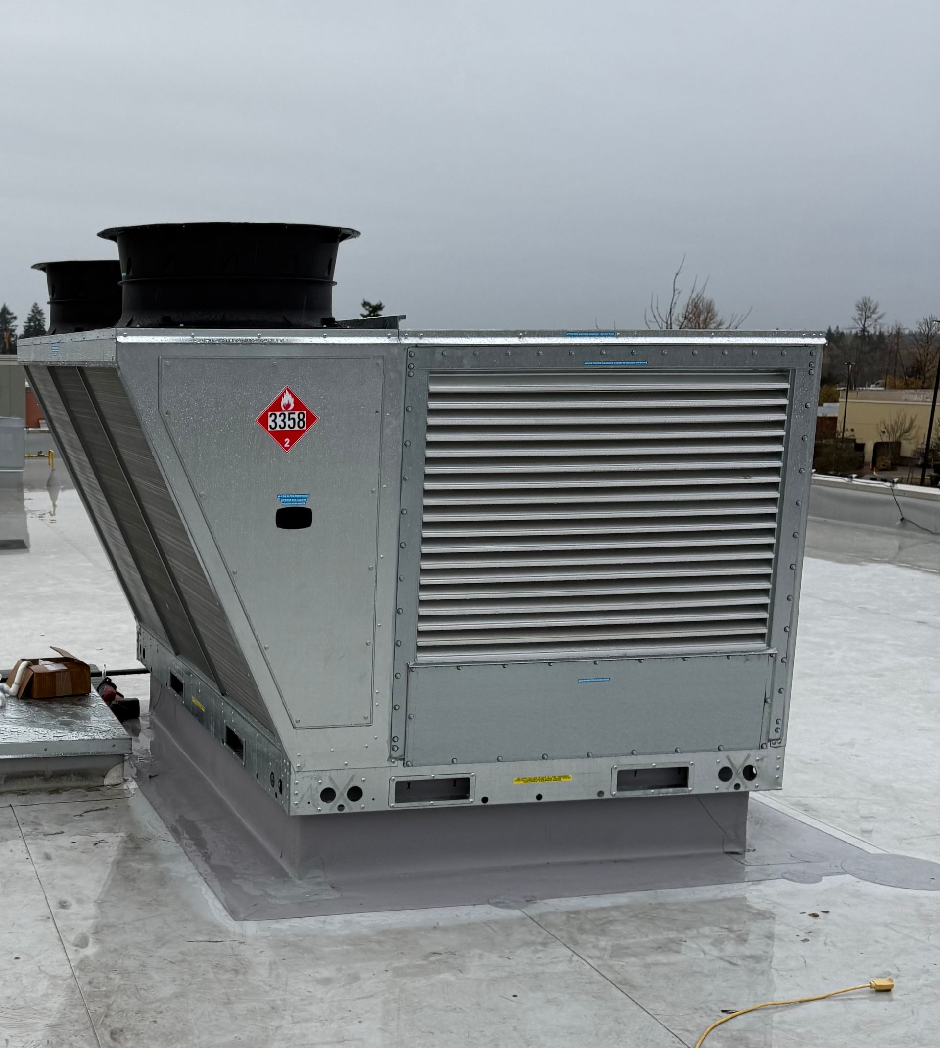 Large silver rooftop HVAC unit with vents on a flat roof under an overcast sky