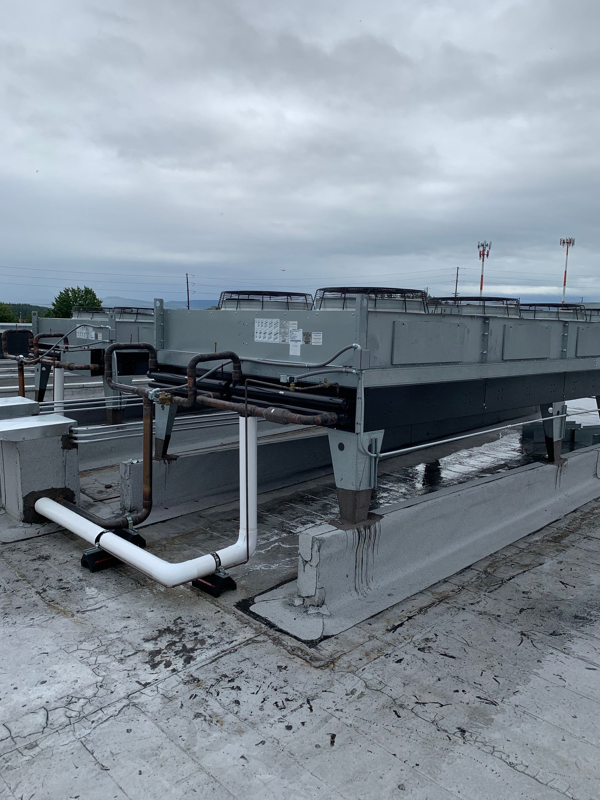 Rooftop HVAC units and white piping on a flat commercial roof under a cloudy sky