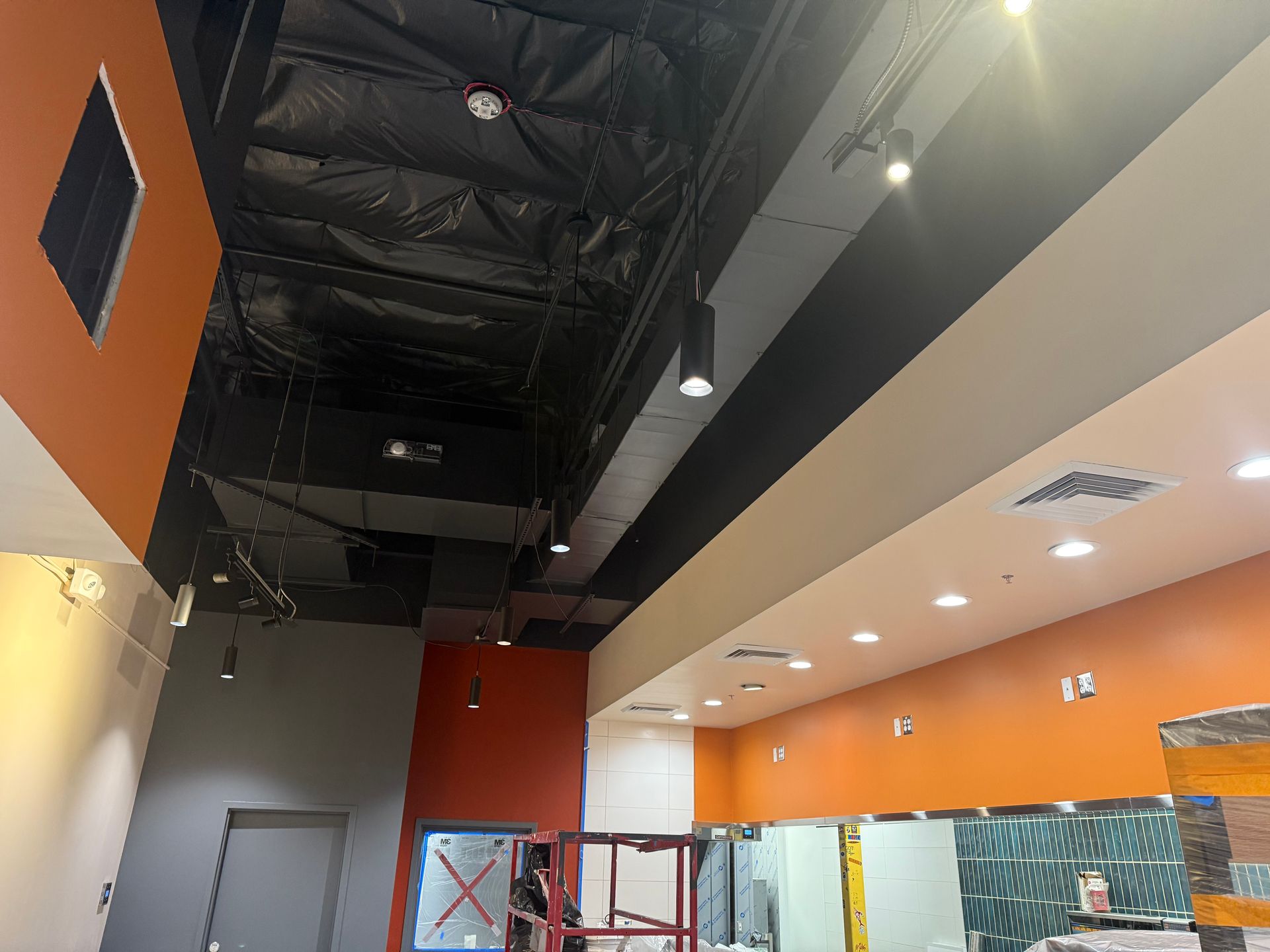 Partially finished indoor space with orange and gray walls, high ceiling, and work scaffolding