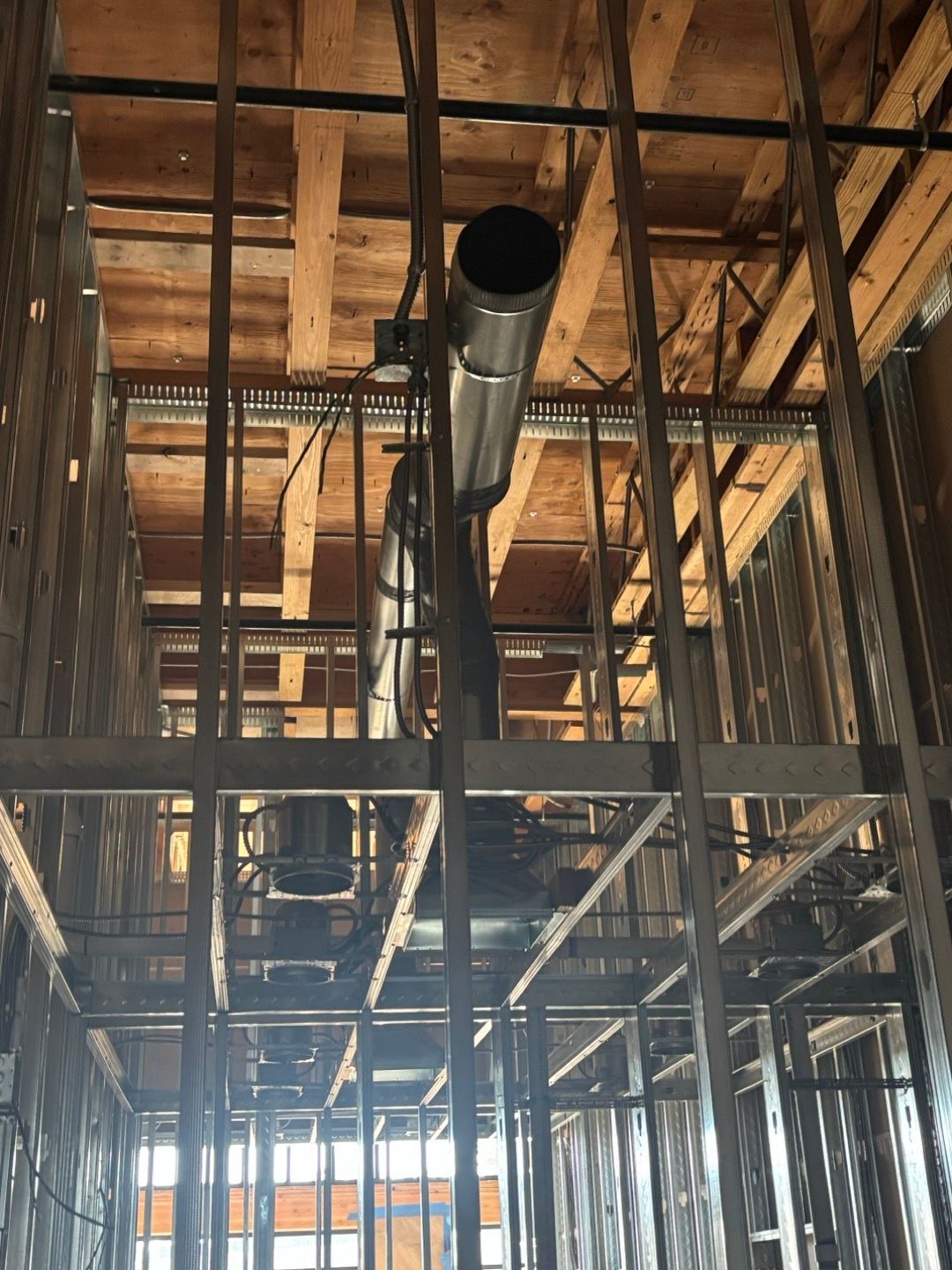 Construction site interior with exposed wooden framing and a large metal HVAC duct overhead.