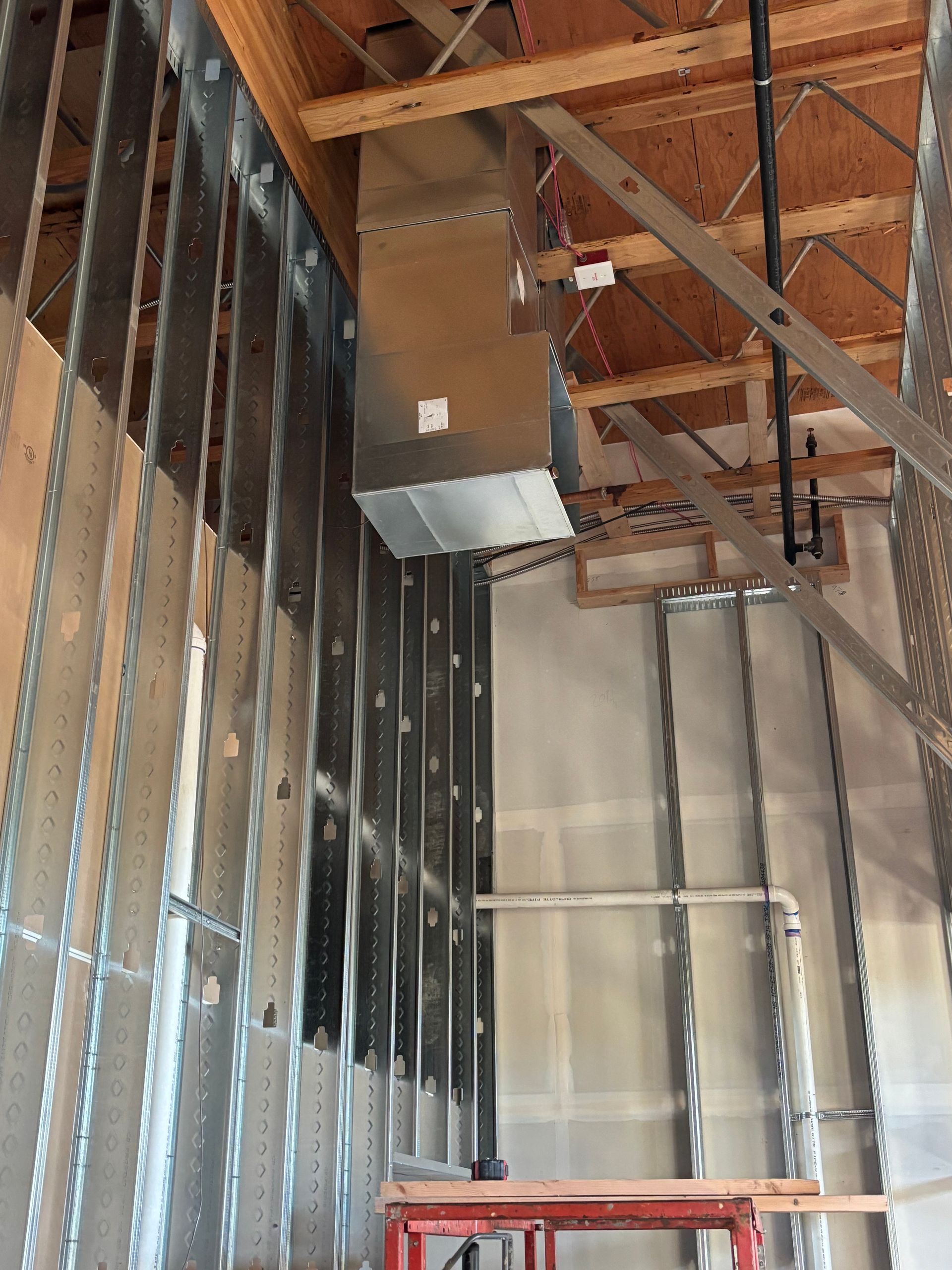 Interior of a construction site with exposed metal studs, wood rafters, HVAC ducting, and a ladder.