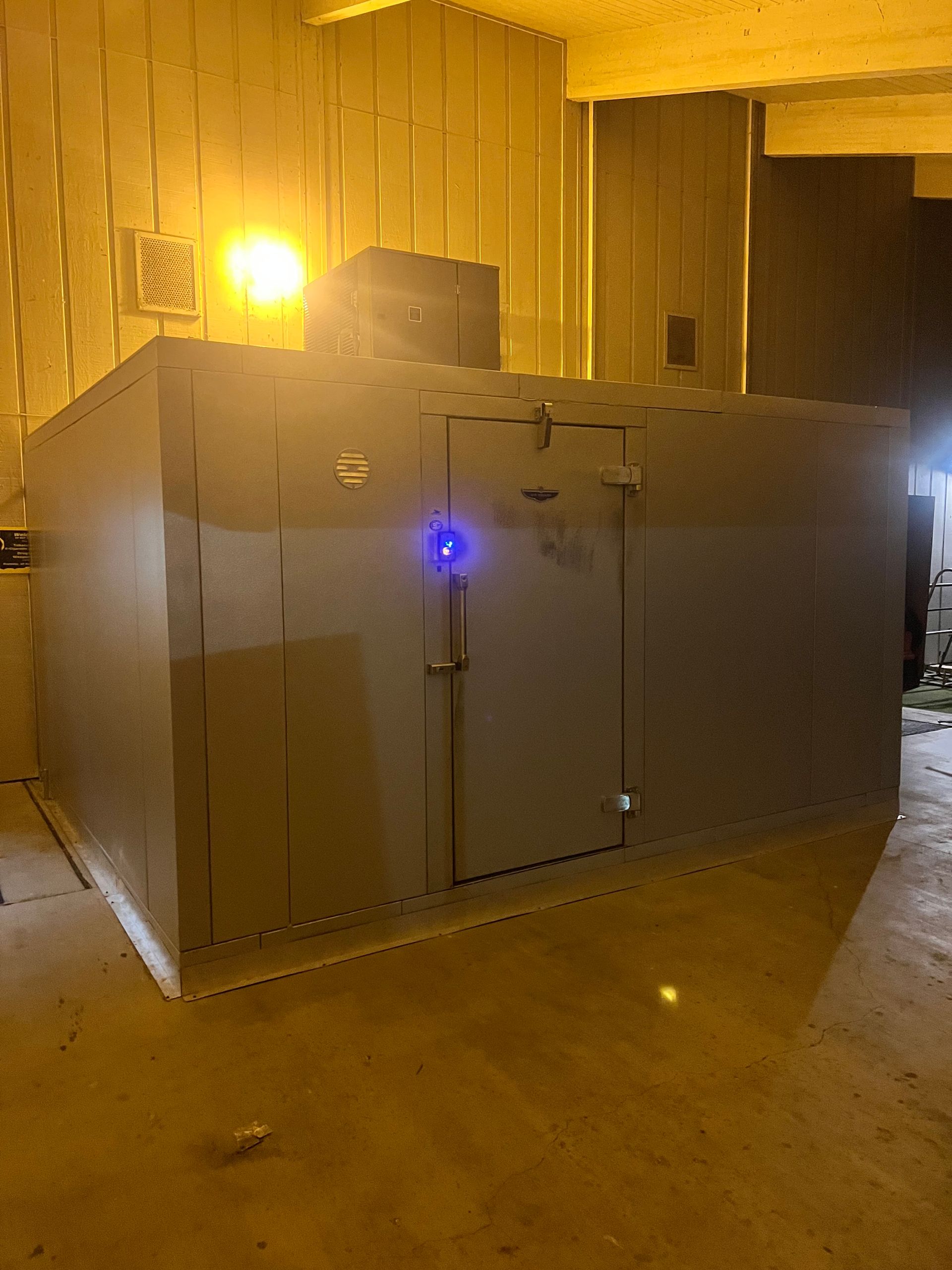 Large gray industrial unit with a blue indicator light in a warehouse, lit by a bright yellow lamp.