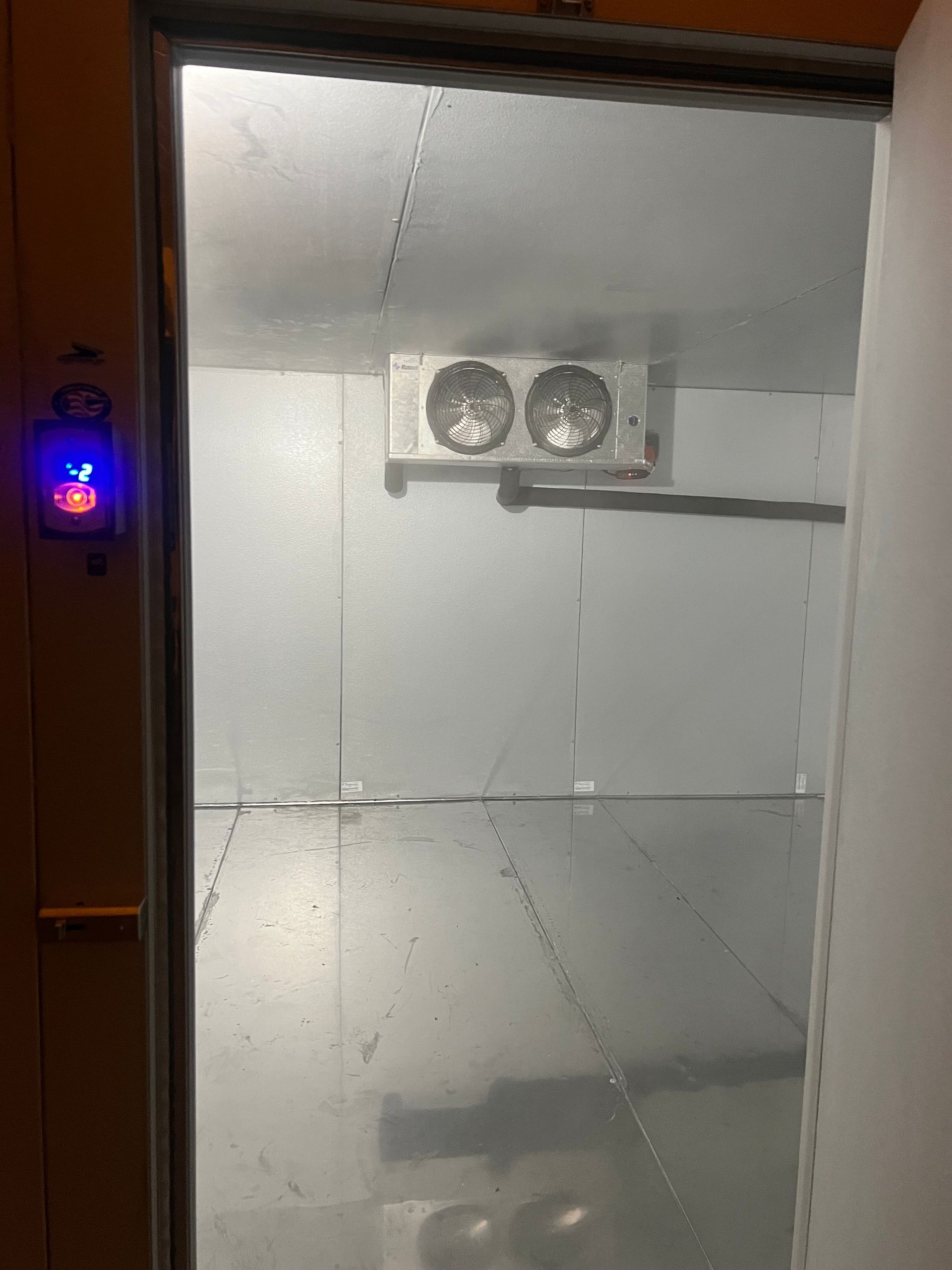 Frosted glass door to a cold storage room with a ceiling fan and wall-mounted control panel.
