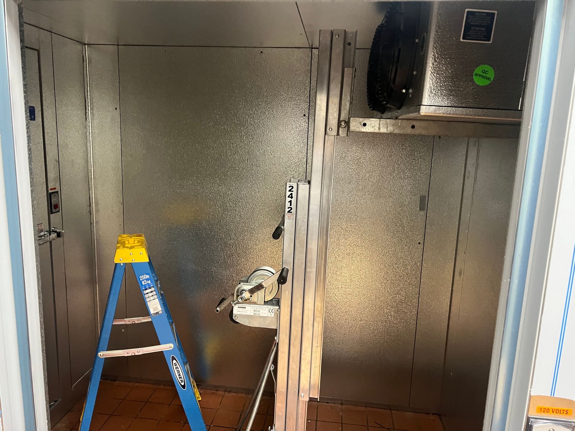 Blue ladder in a metallic HVAC/utility shaft with ductwork and stacked planks.