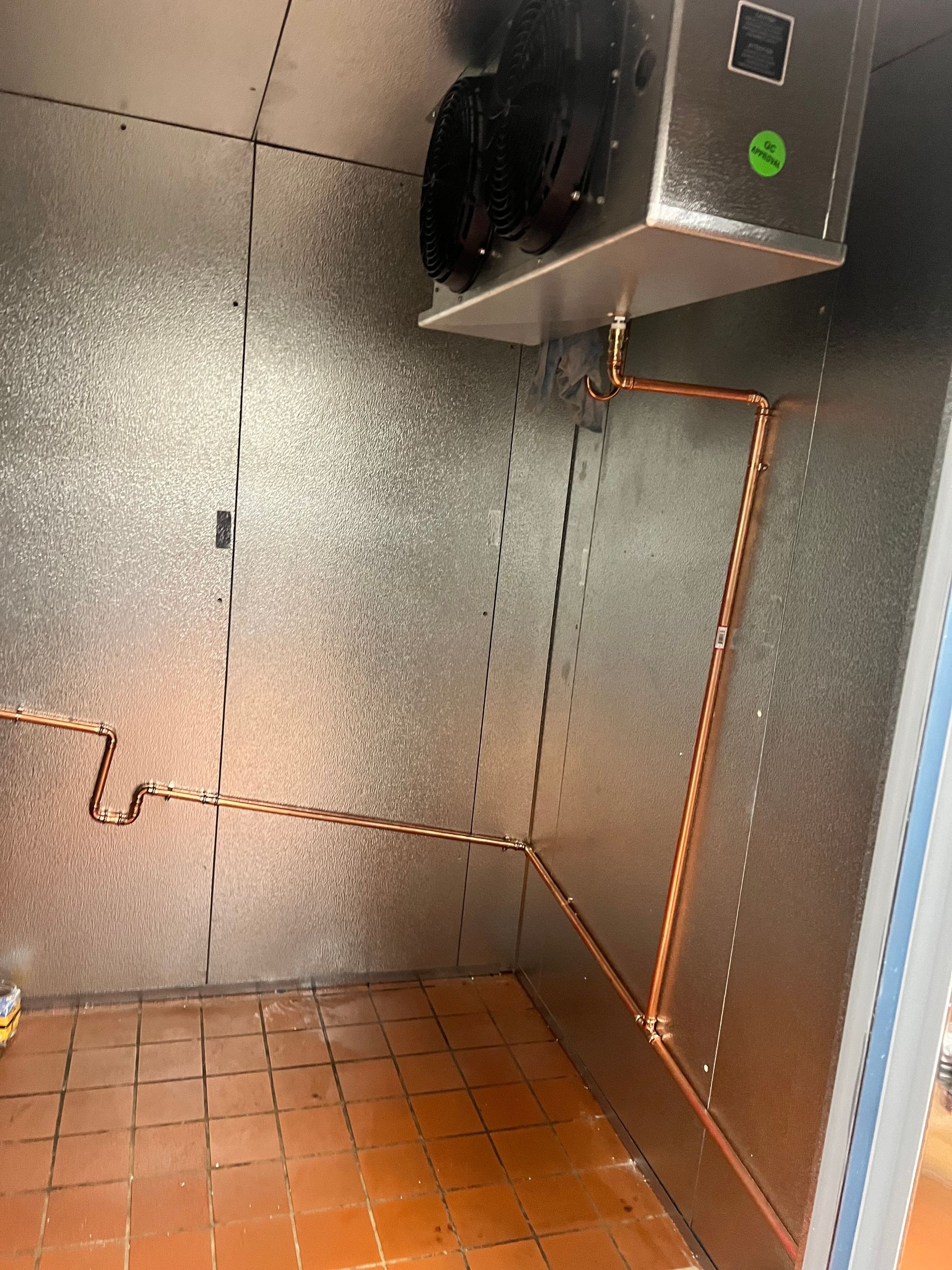 Small stainless steel utility room with copper piping, tiled floor, and wall-mounted equipment.