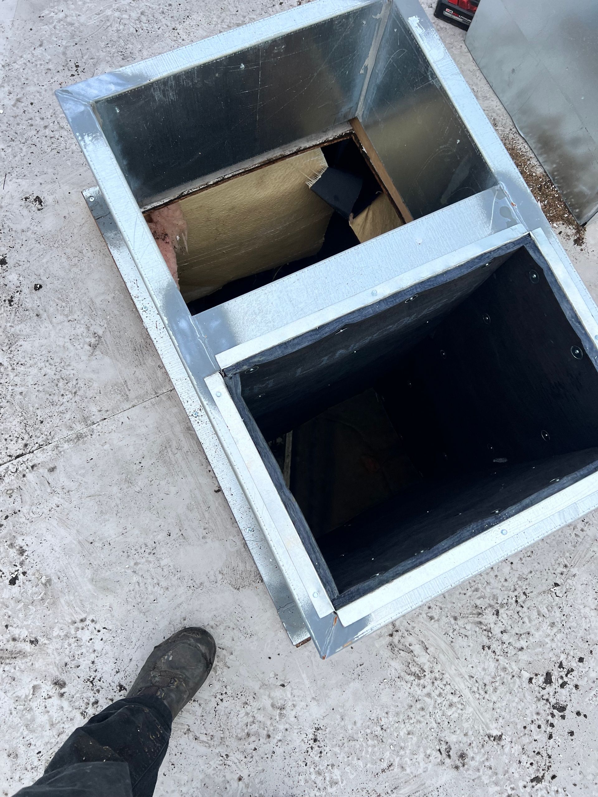 Top-down view of two metal floor openings, one dark, on a concrete surface with a shoe visible at bottom left