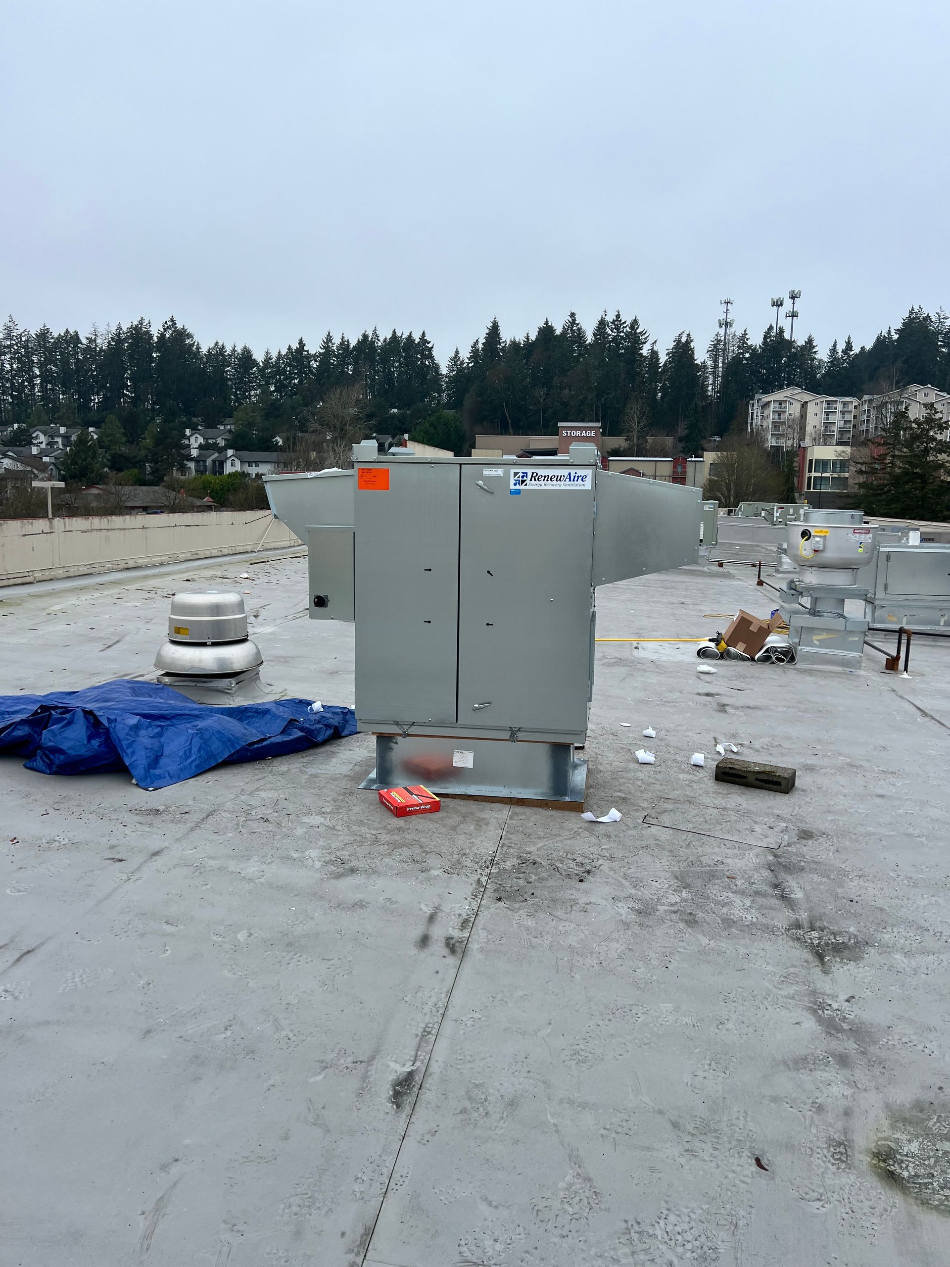 Outdoor utility equipment on a wet concrete lot, with scattered debris and a blue tarp under an overcast sky