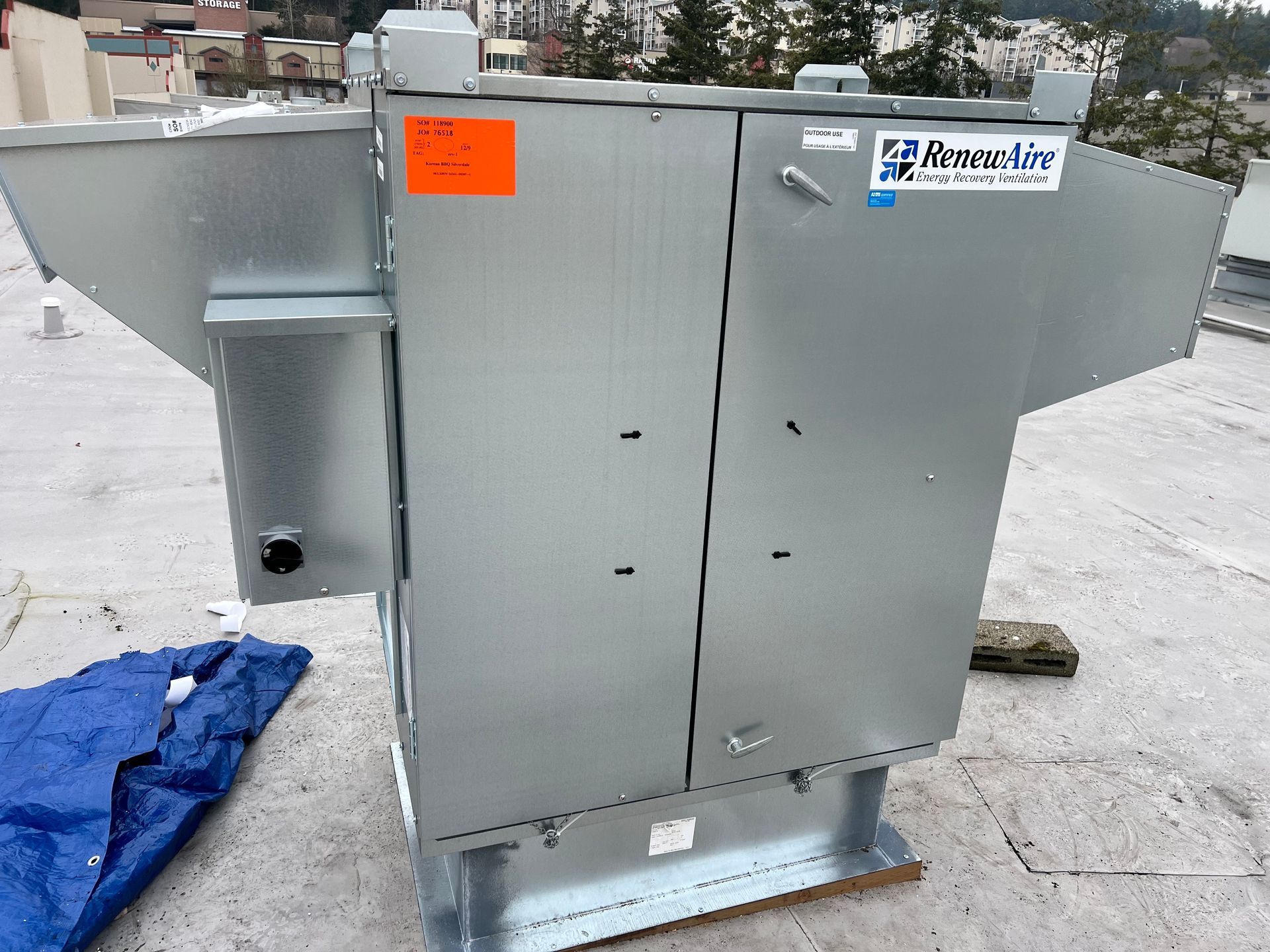 Gray rooftop HVAC unit with a small rooftop vent and orange warning label on a snowy surface