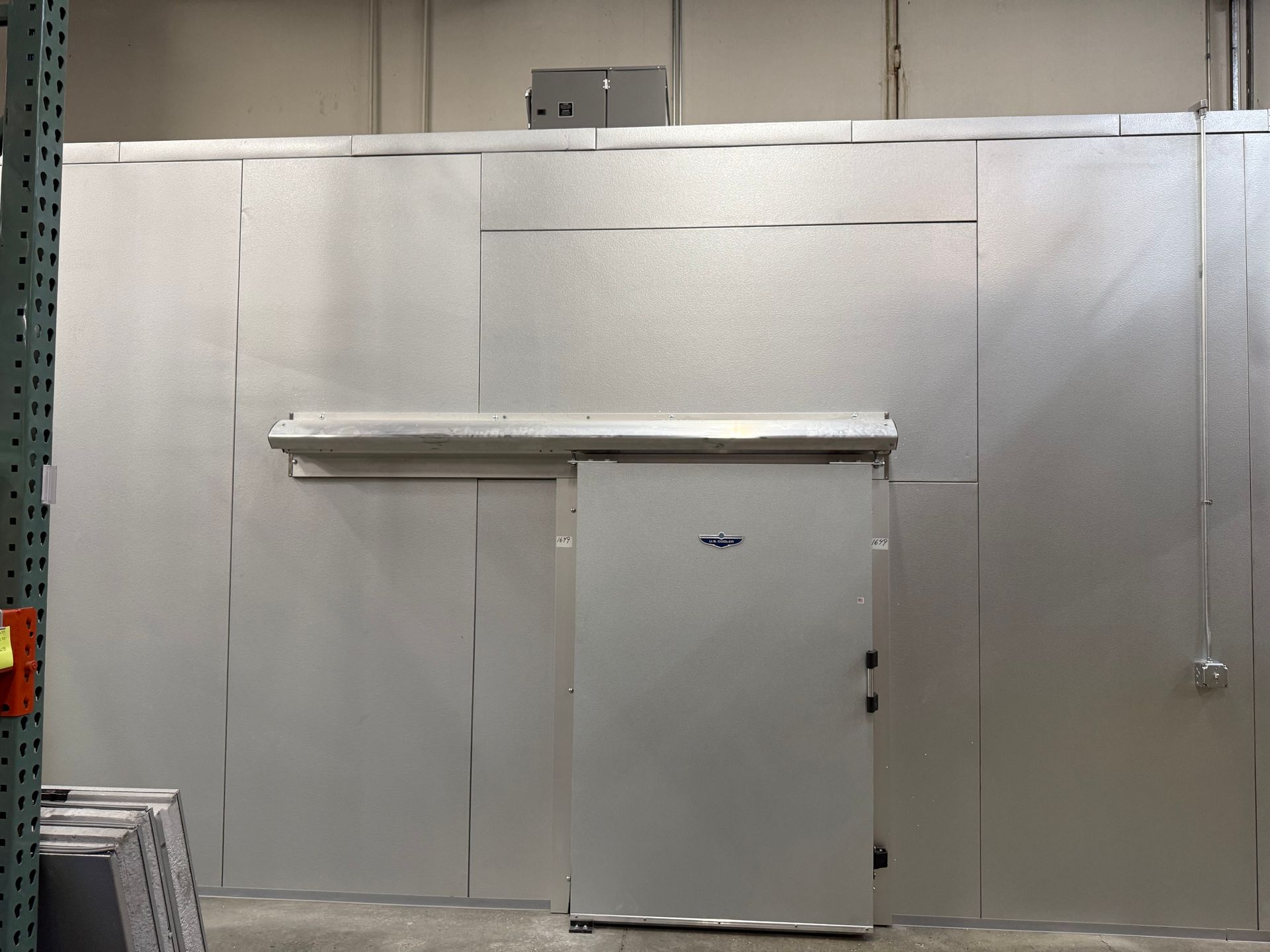 Industrial metal wall with a centered gray door and overhead vent in a warehouse-like room