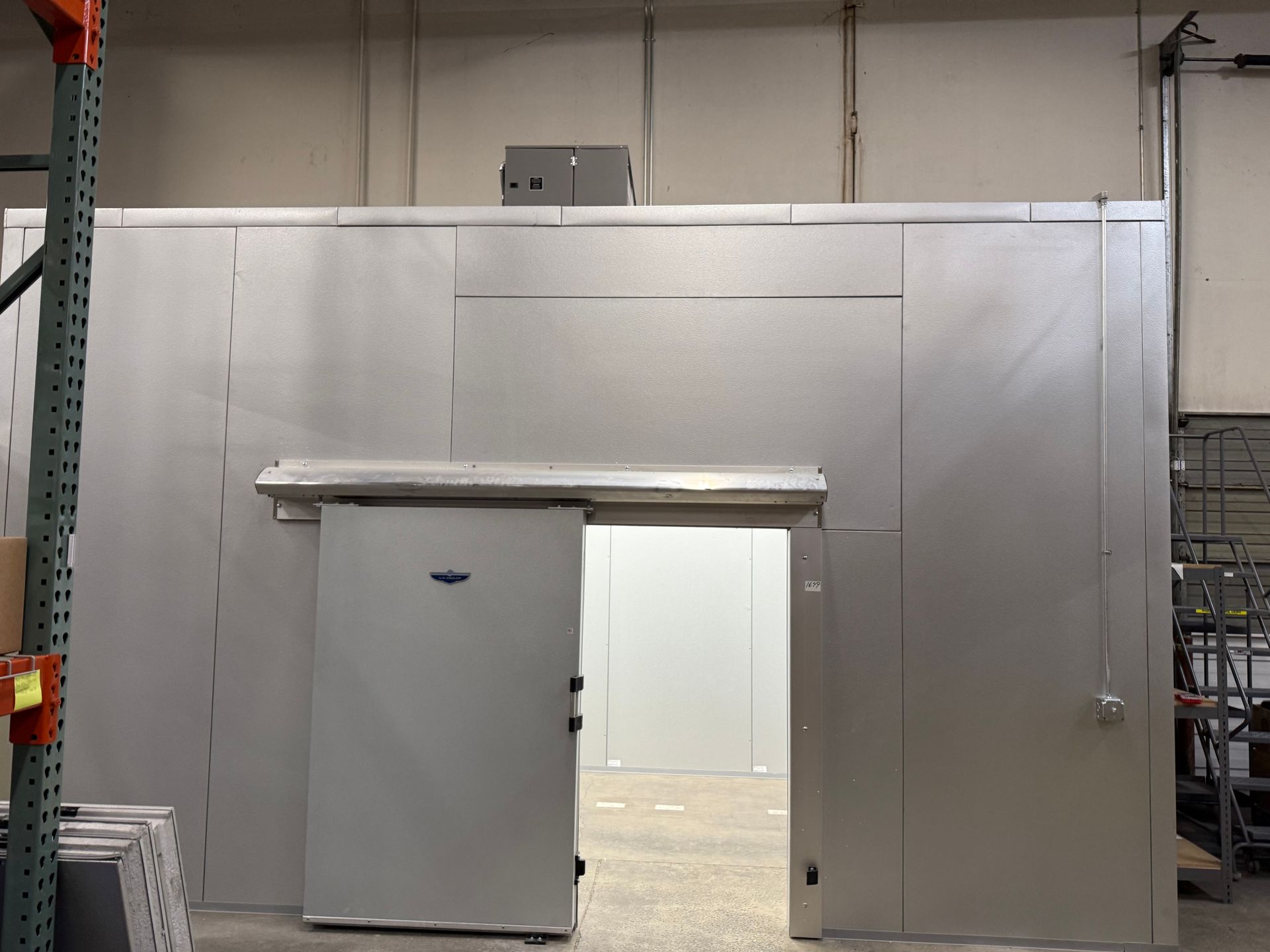 Large gray industrial sliding door in a warehouse wall, partly open to a bright interior room.