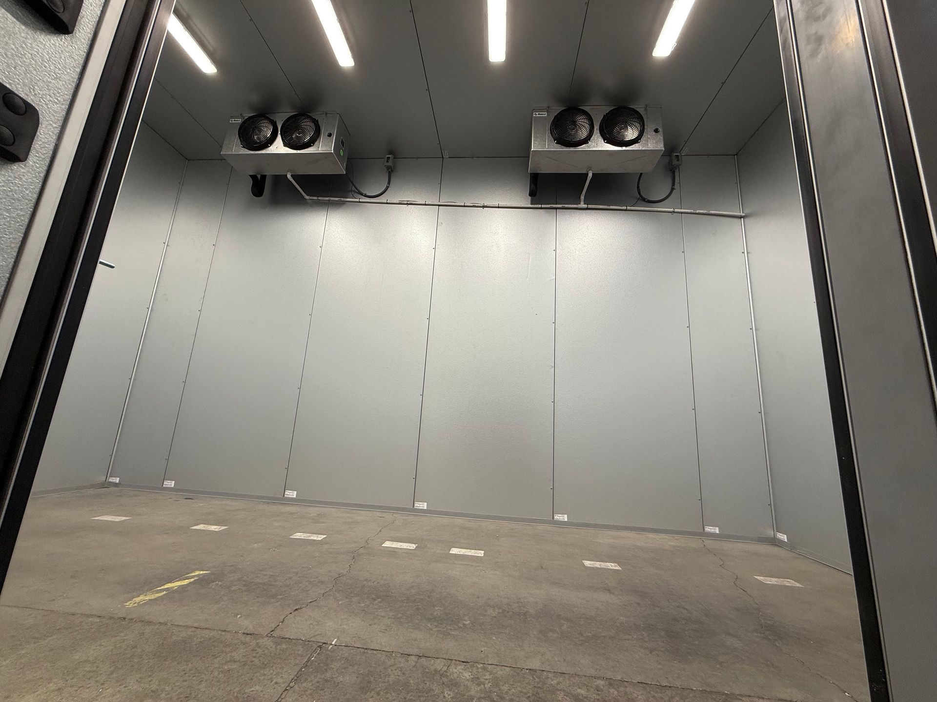 Empty gray industrial room with ceiling fans, fluorescent lights, and a concrete floor