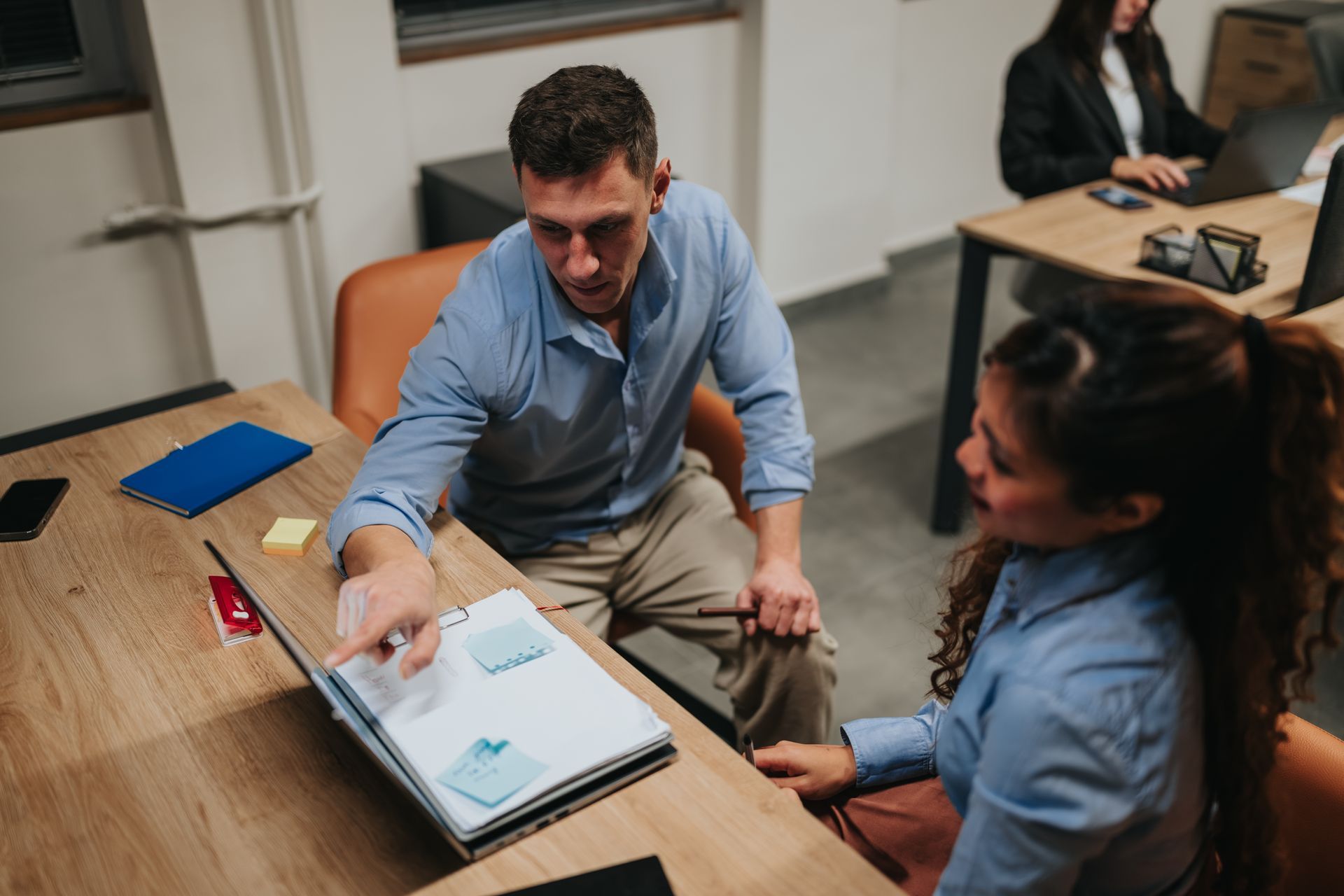 Two business teammates review and point at documents on a wooden desk.