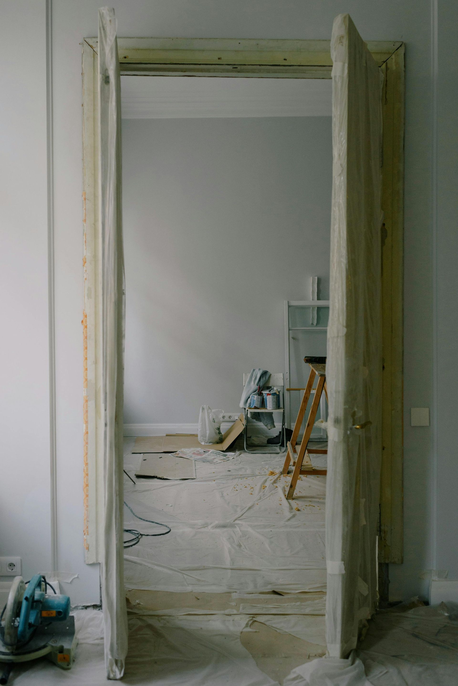 Doorway in renovation, revealing interior with debris, ladder, and tools; pale walls.