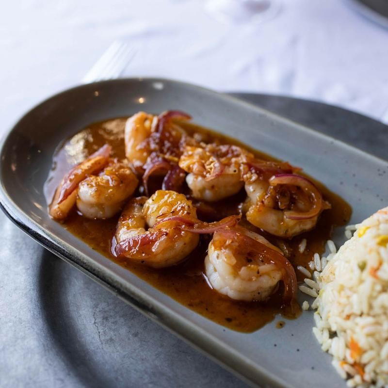 Shrimp in brown sauce on a dark plate beside a mound of rice