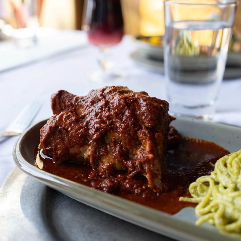 Plated red sauced meat with noodles on a table, with a glass of water in the background