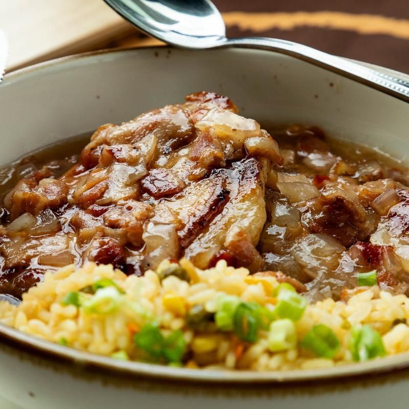 Close-up of a bowl of glazed meat with sautéed onions and rice, served with a spoon