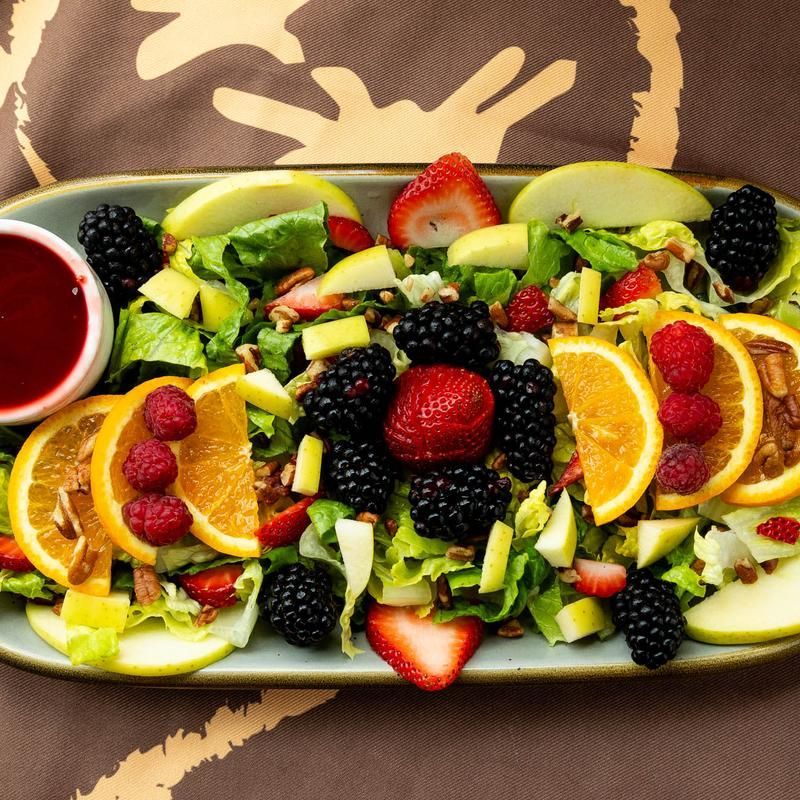 Fresh fruit salad with oranges, berries, apples, and avocado on a platter with red sauce on the side