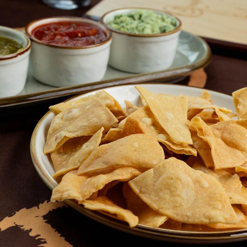 Bowl of tortilla chips with three dipping sauces in the background