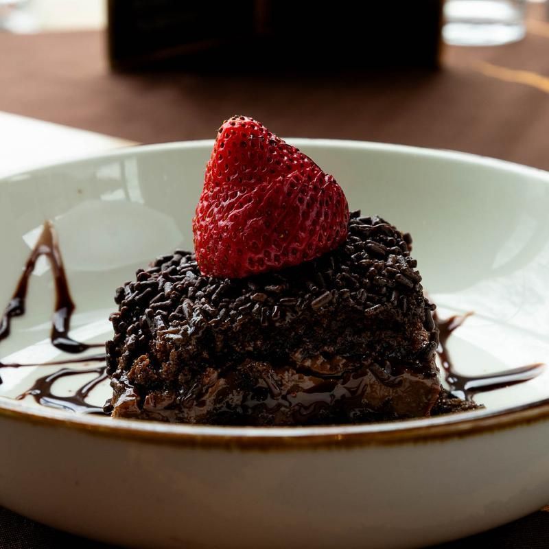 Chocolate dessert topped with a strawberry on a white plate with chocolate sauce drizzles