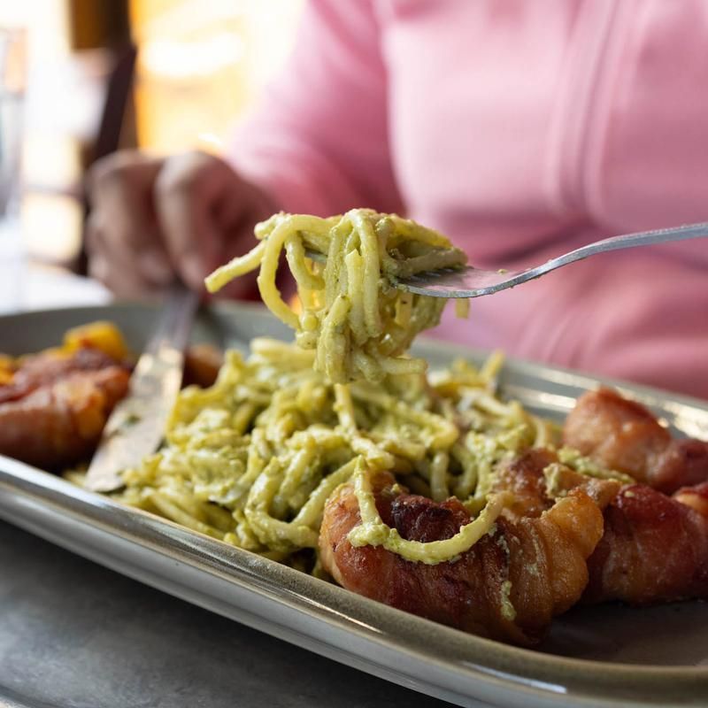 Person lifting green pasta from a tray with a fork in a restaurant setting