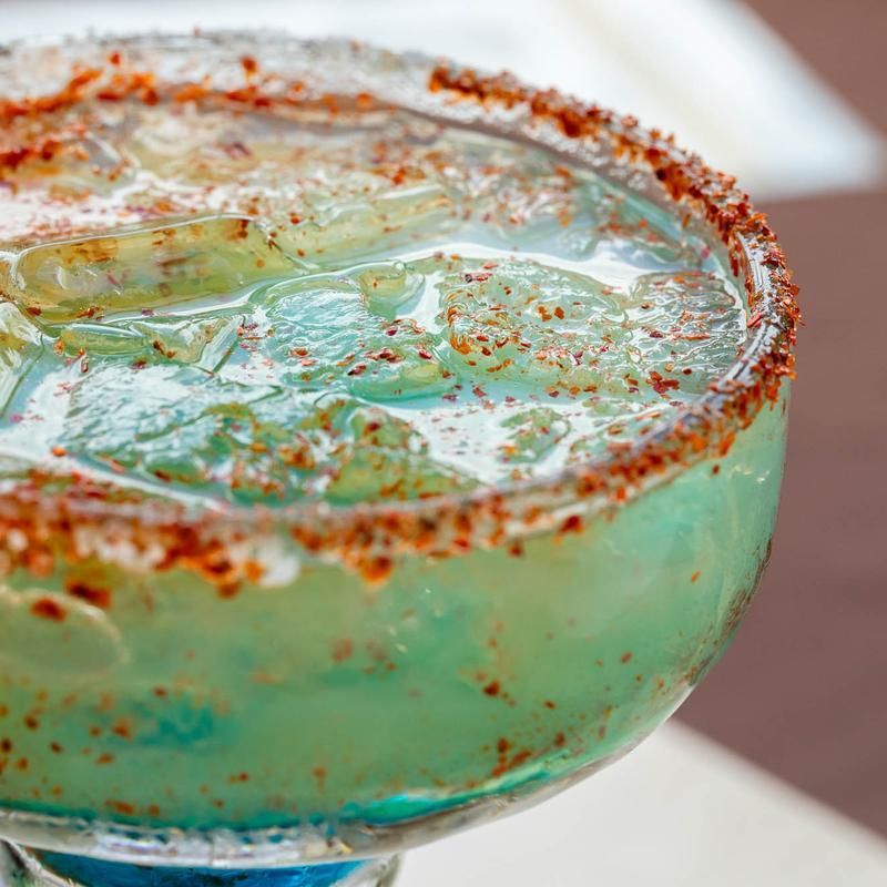 Close-up of a turquoise cocktail in a salt-rimmed glass with a lime wedge and red chili seasoning