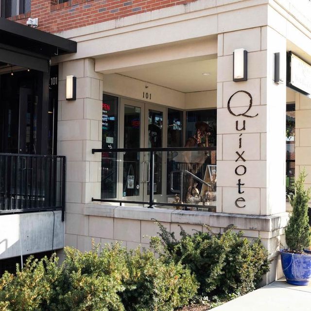 Entrance of Quixote restaurant with black railing, beige stone facade, and potted greenery