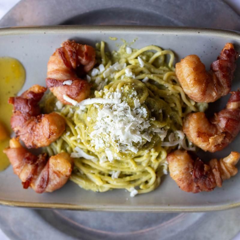 Pesto pasta topped with grated cheese and surrounded by bacon on a rectangular plate