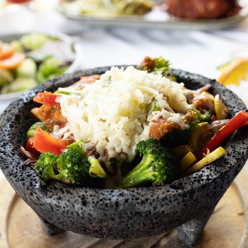 Black bowl of rice and mixed vegetables, including broccoli and red peppers, on a table