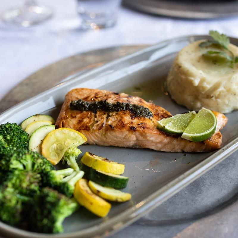 Grilled salmon with broccoli, zucchini, and lime on a metal tray, with a side of mashed potatoes