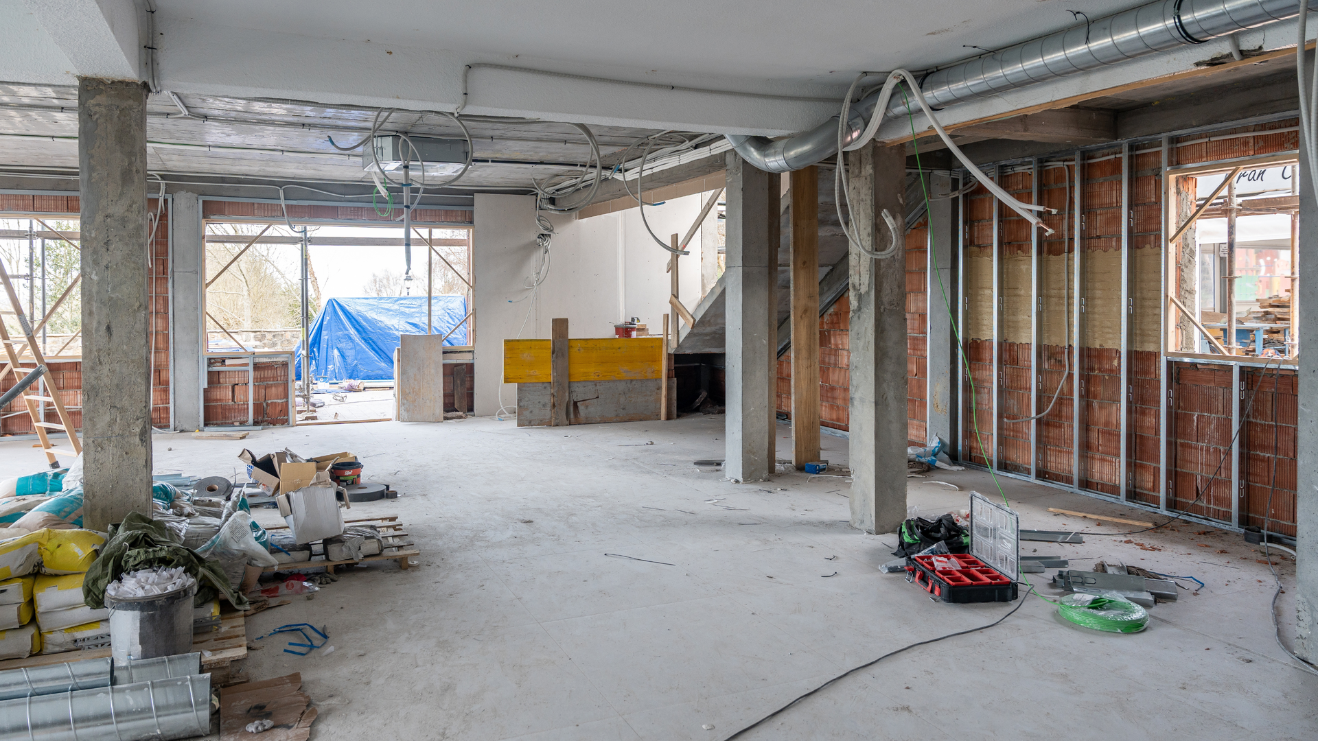 Workers on scaffolding installing steel beams inside an unfinished industrial building.