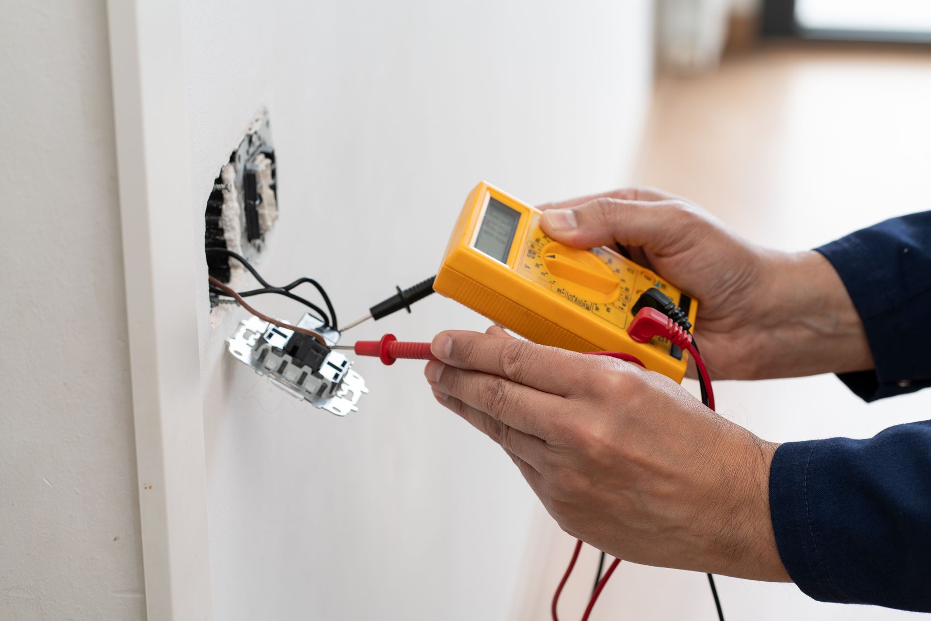 Electrician testing a wall outlet with a multimeter during electrical repair