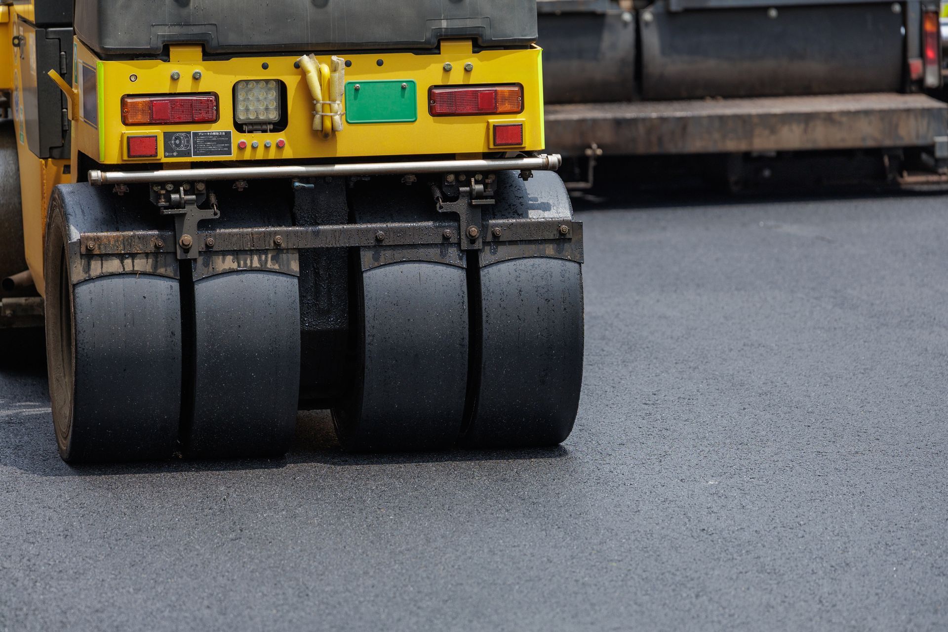 Close-up of a yellow road roller’s rear wheels compacting fresh asphalt on a street Close-up of a yellow road roller’s rear wheels compacting fresh asphalt on a street