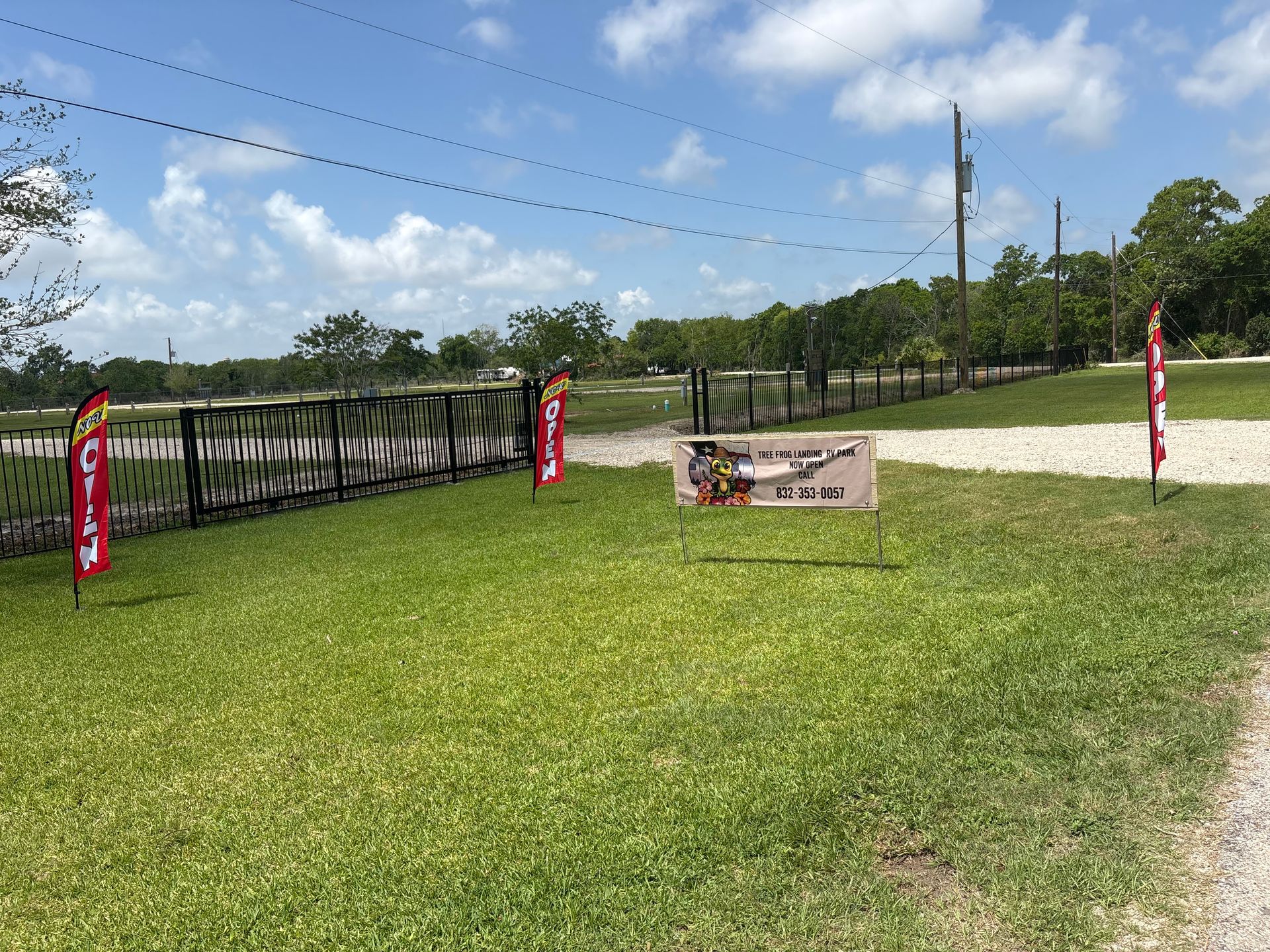 Rural roadside entrance with a black gate, red banners, and a small sign under a sunny blue sky
