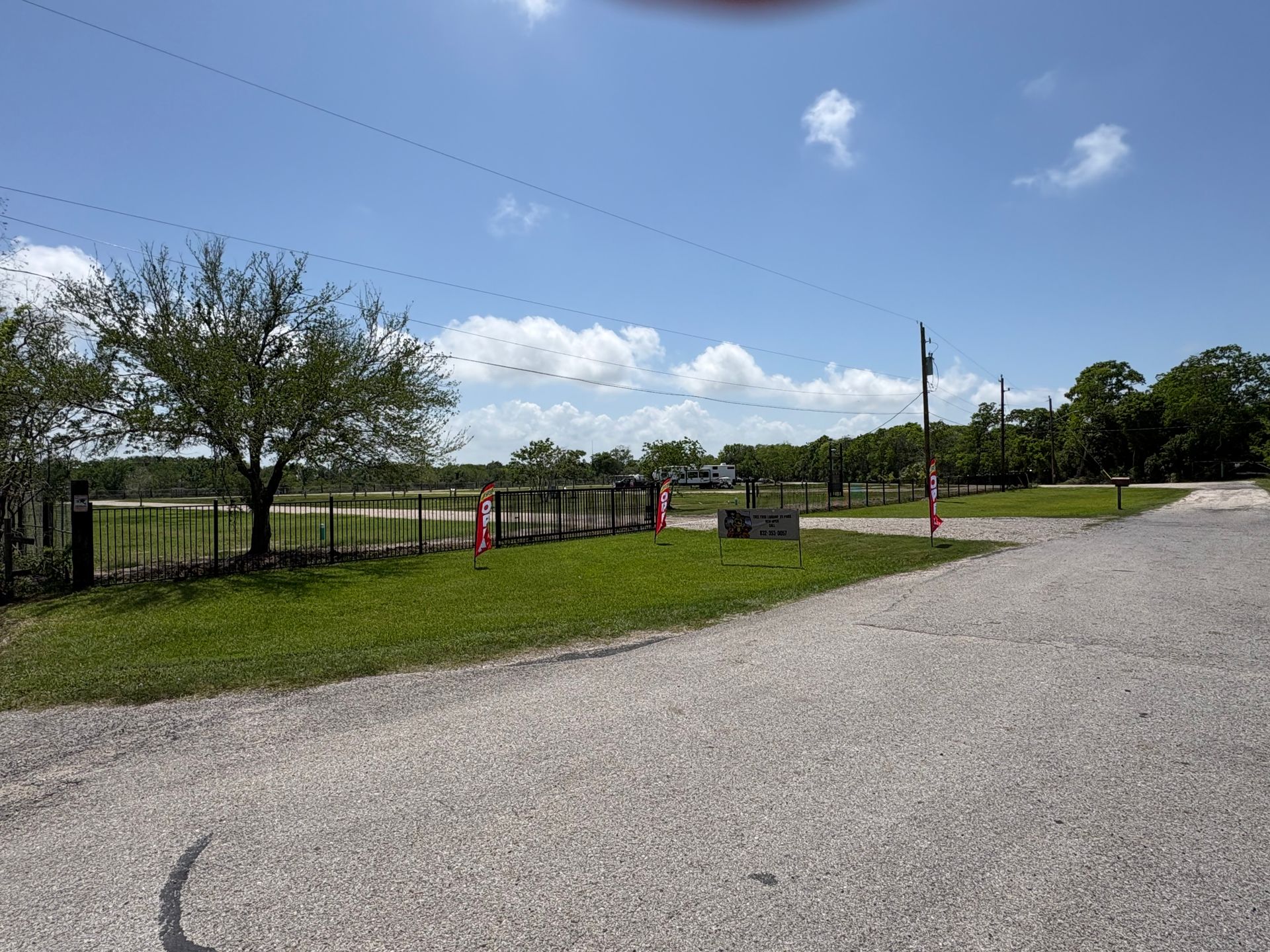 Gravel road beside a fenced grassy field under a blue sky with scattered clouds