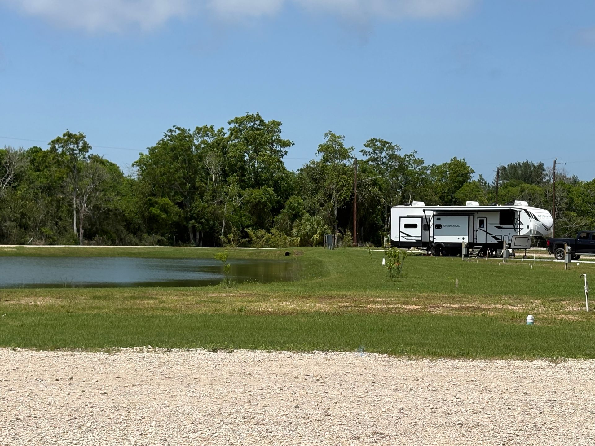 RV parked by a small pond with trees and blue sky in the background