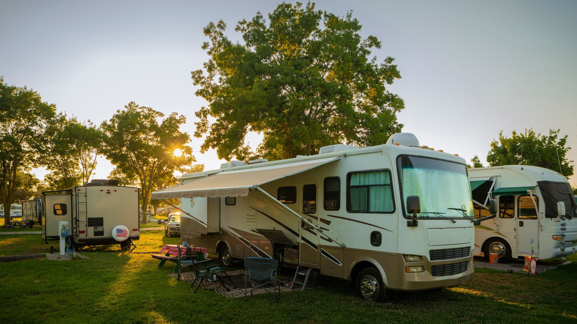 RVs parked on a grassy campsite at sunset, with trees and warm golden light.