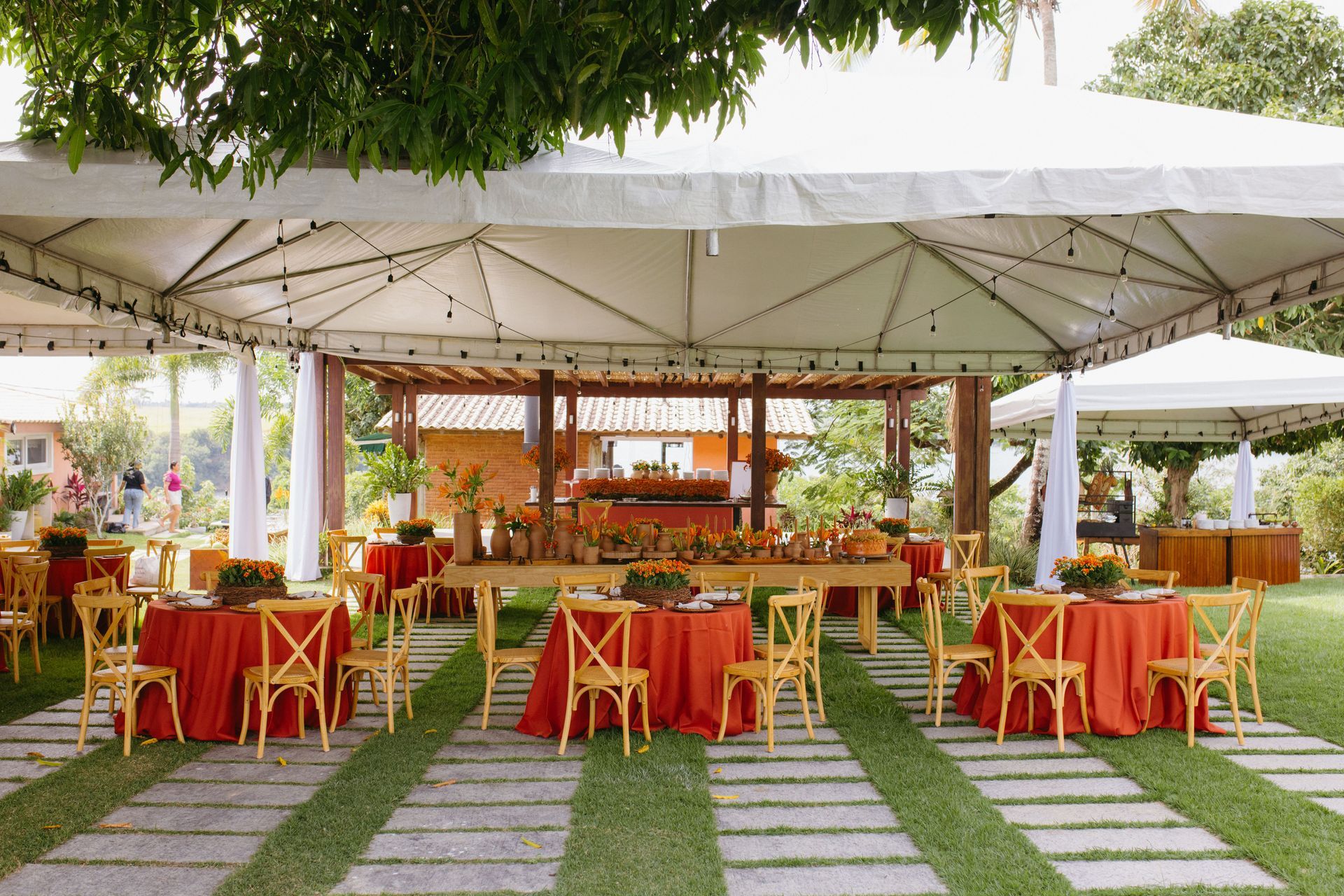 Outdoor banquet setup with red chairs and tables under white tents on a grassy lawn