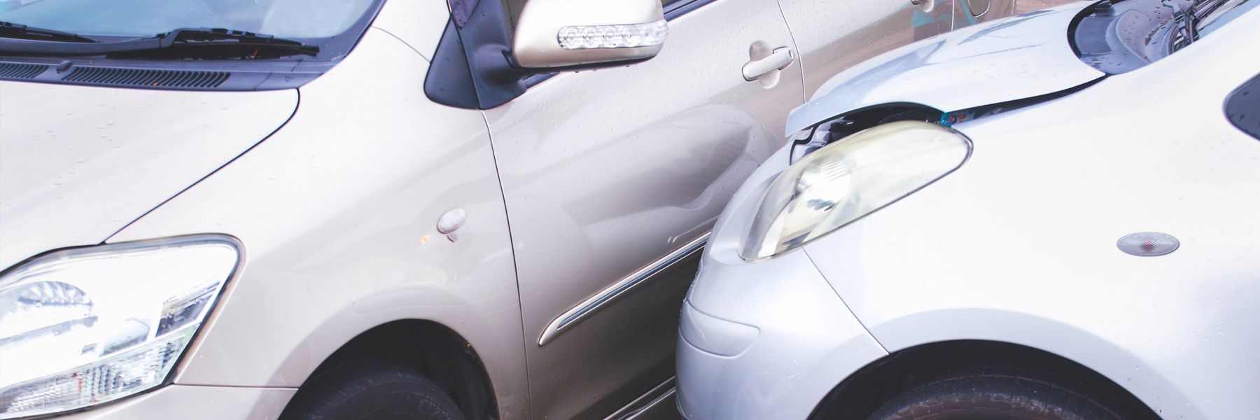 Two cars involved in a collision; one car's front damaged, the other car's side dented.