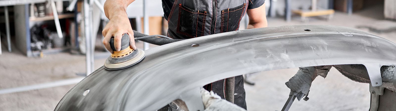 Person sanding a car bumper in a workshop.